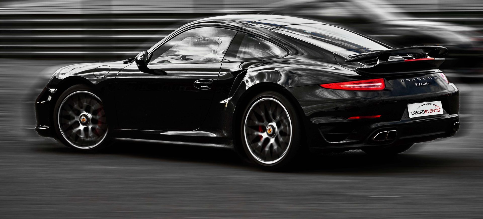 Porsche 911 Turbo noire en plein filé latéral sur la piste, traînées de vitesse en arrière-plan désaturé