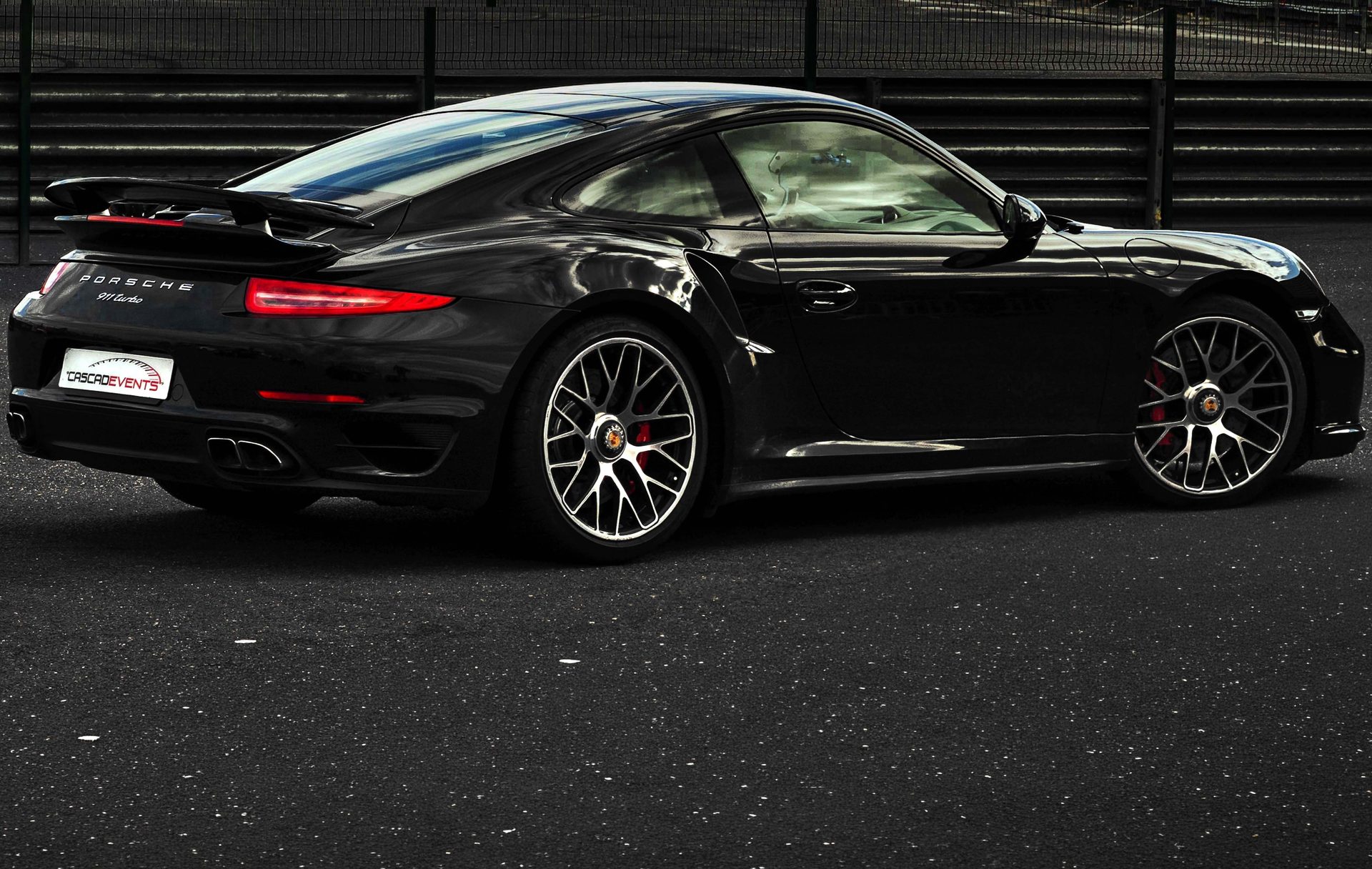 Porsche 911 Turbo noire vue de trois quarts arrière à l'arrêt sur le tarmac, jantes turbines noires brillantes