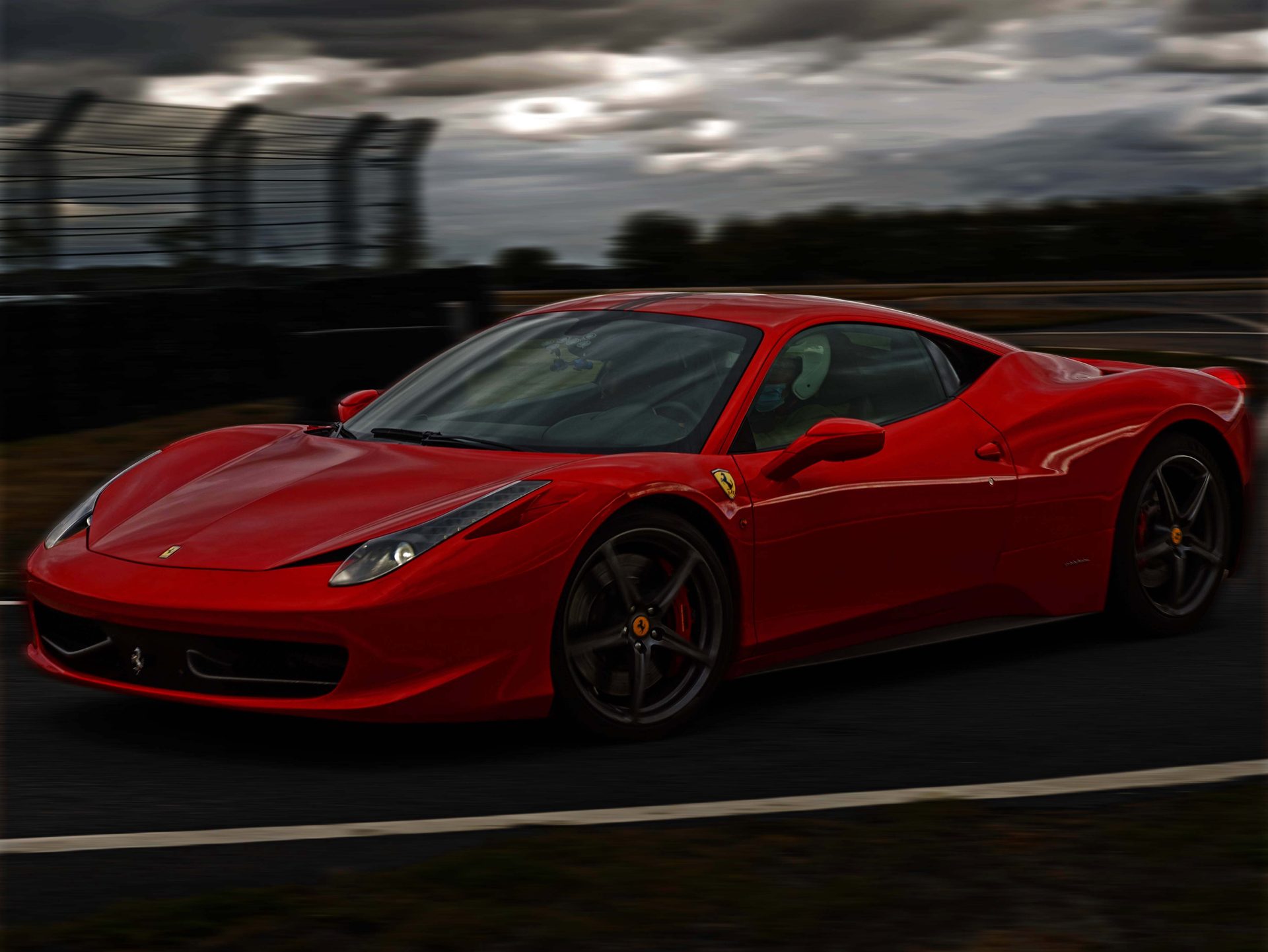 Ferrari 458 Italia rouge en filé latéral sur la piste, ciel orageux nuancé en arrière-plan