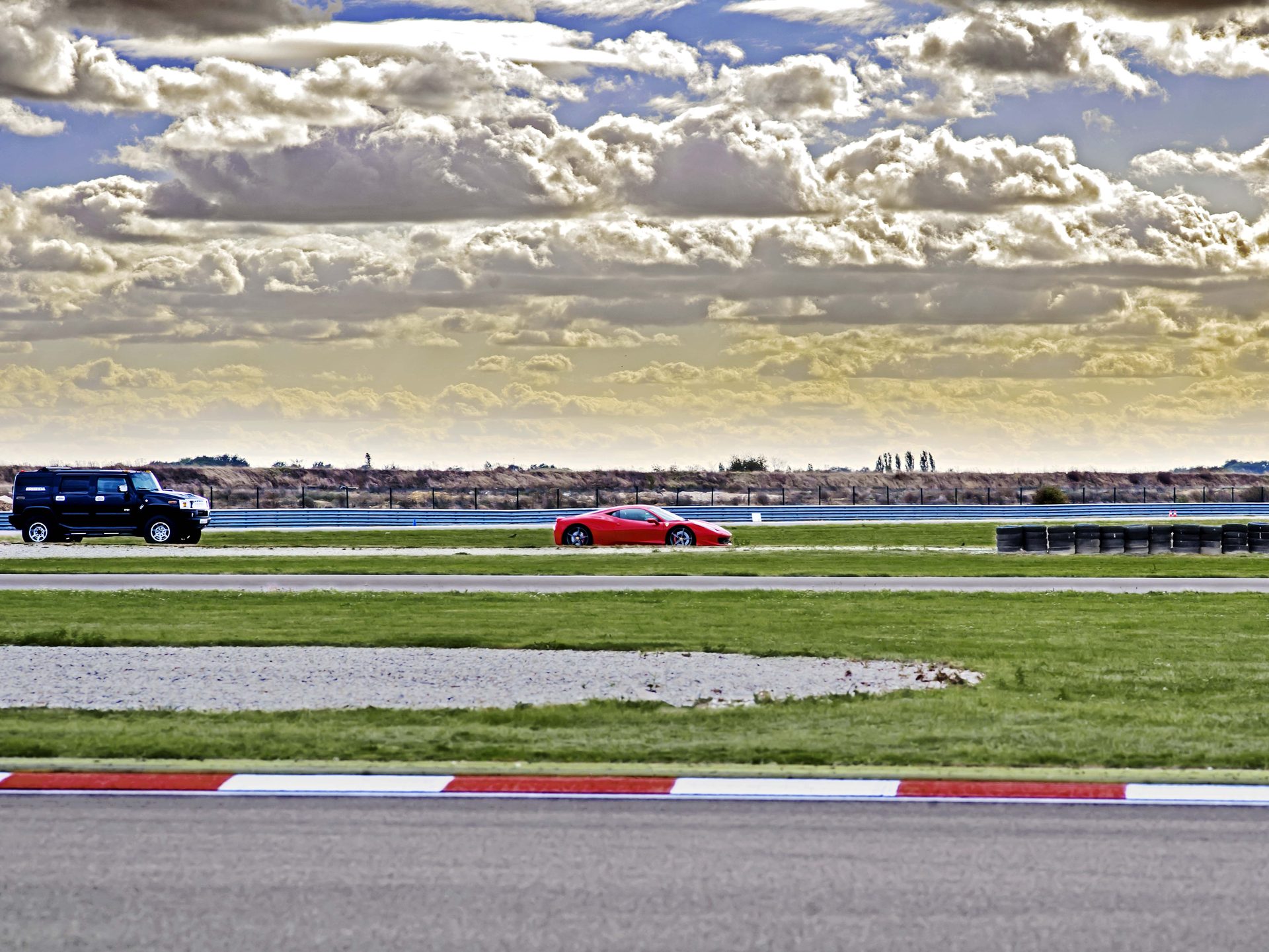 Vue panoramique du circuit : Hummer H2 noir et Ferrari 458 rouge en piste, ciel cumulus reconstruit pour donner de la profondeur