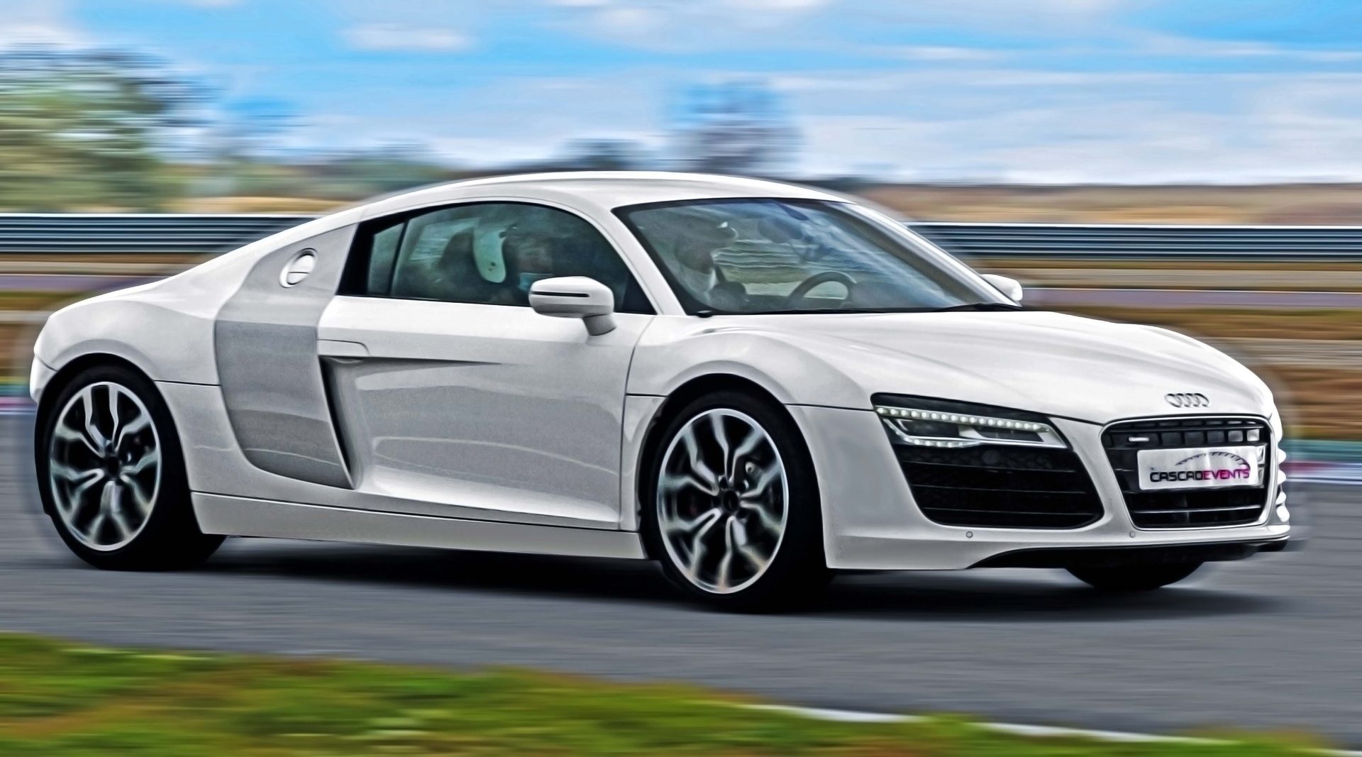 Audi R8 V8 blanche en filé latéral sur le circuit, plaque Cascadevents visible, traînées de filé reverdies en arrière-plan