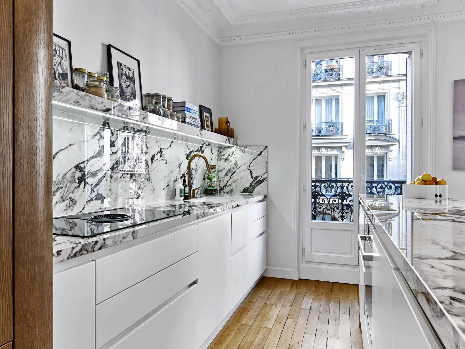 Cuisine en marbre veiné avec robinetterie laiton et vue sur balcon haussmannien