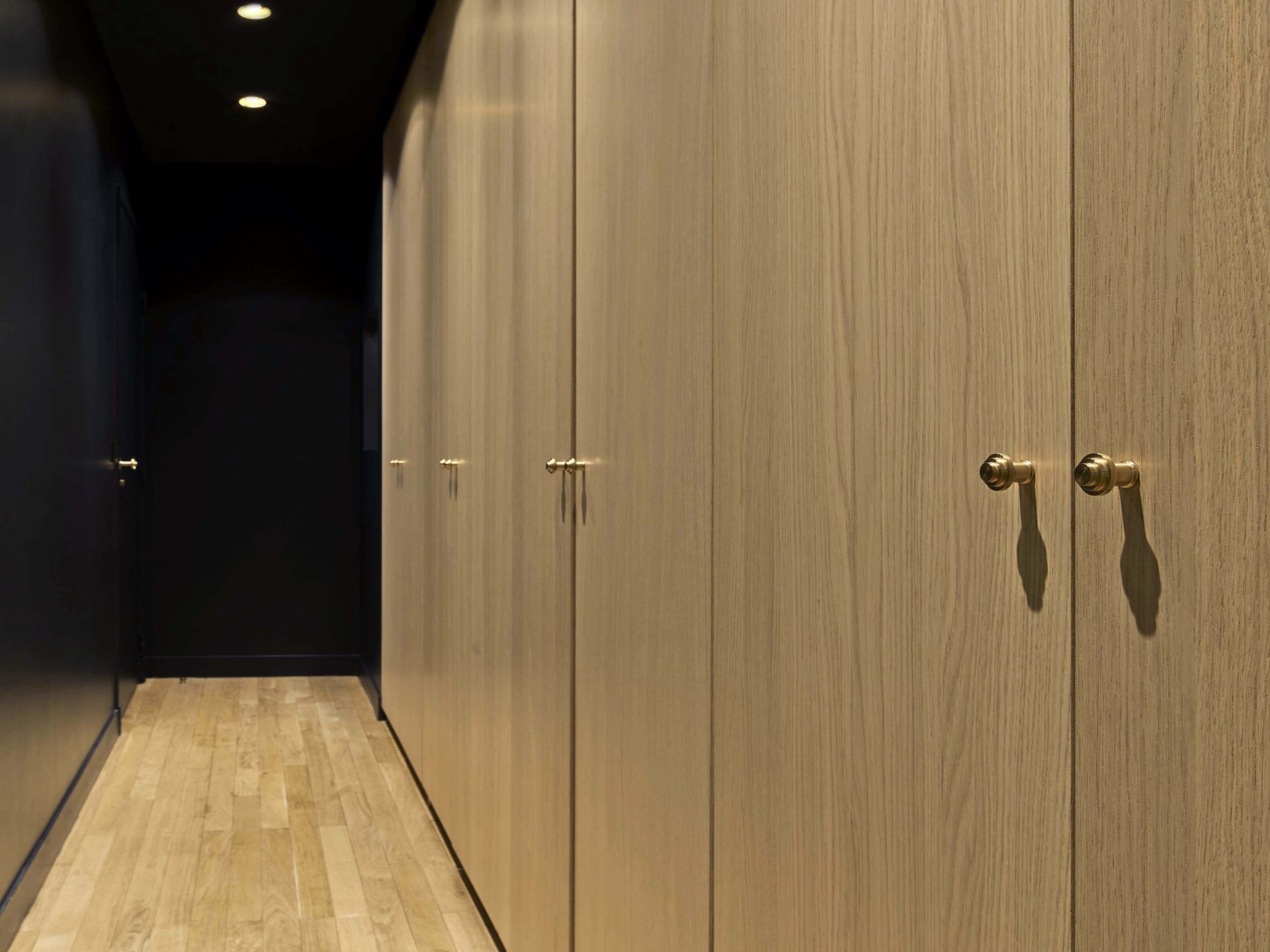 Couloir dressing aux portes en chêne clair, béquilles dorées et plafond noir