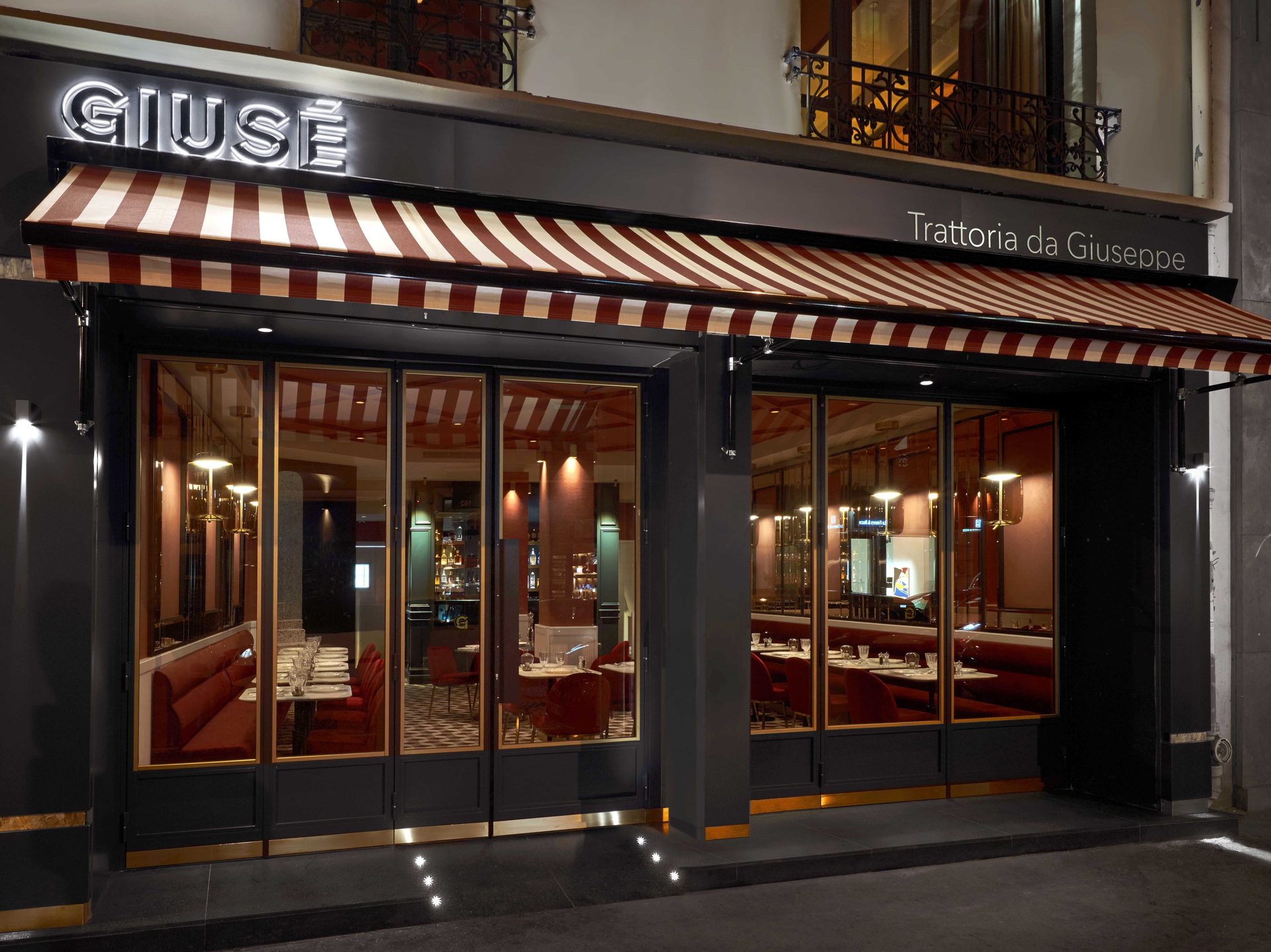 Façade nocturne du Guisé Trattoria da Giuseppe : enseigne lumineuse, store rayé rouge et blanc, verrière sur l'intérieur rouge