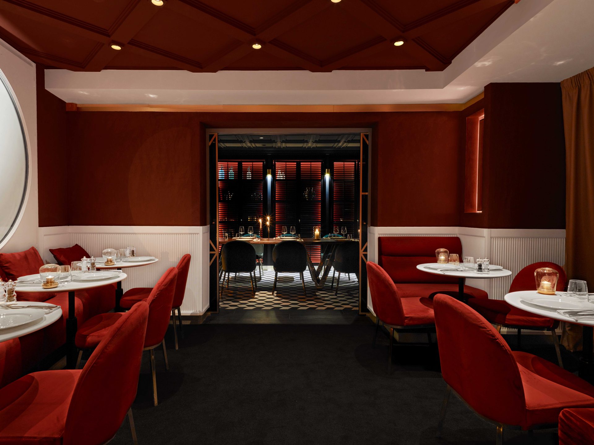 Salle haute rouge — vue axiale frontale sur la table de bois brut du privatif noir baignée de lumière rouge