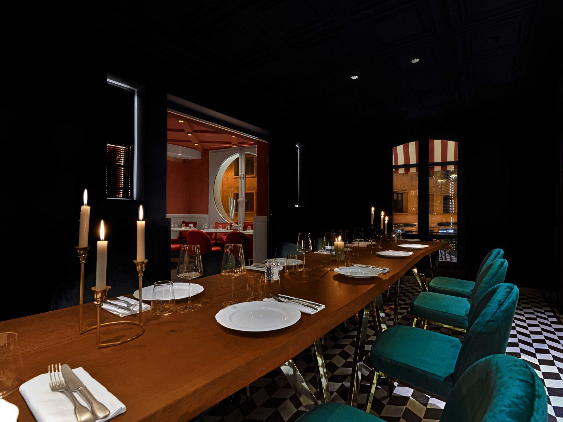 Privatif noir vu en enfilade : table de bois brut, chaises velours bleu canard et volets rouges sur toute la longueur