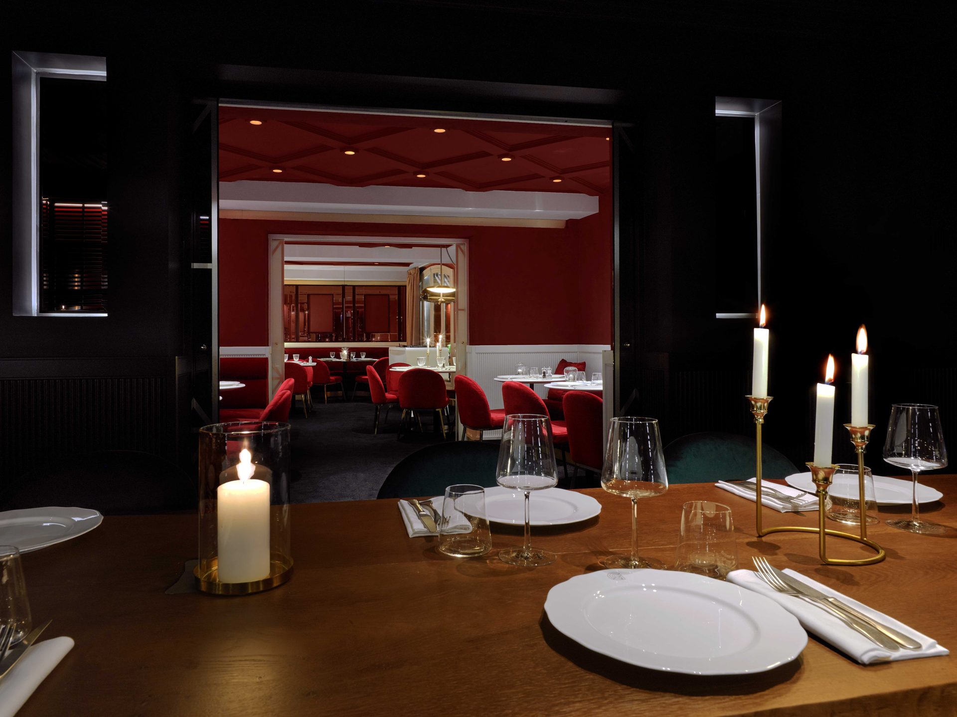 Privatif noir — vue d'ensemble vers les deux salles rouges en enfilade en arrière-plan, candélabres allumés sur la table de bois brut