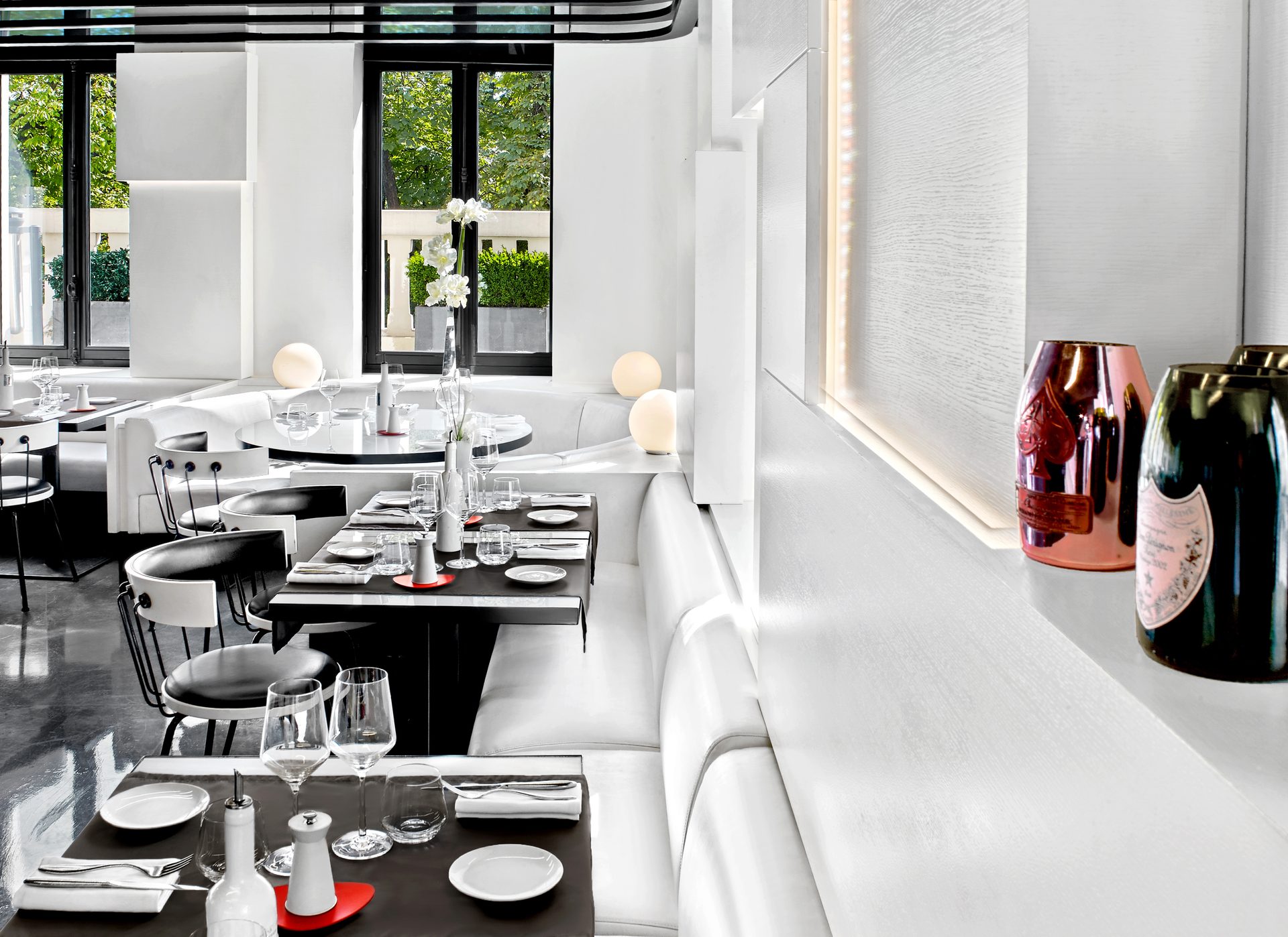 Nolita Paris — vue 02 — perspective de salle vers fenêtre, table dressée au premier plan et magnums Armand de Brignac et Dom Pérignon dans niche éclairée