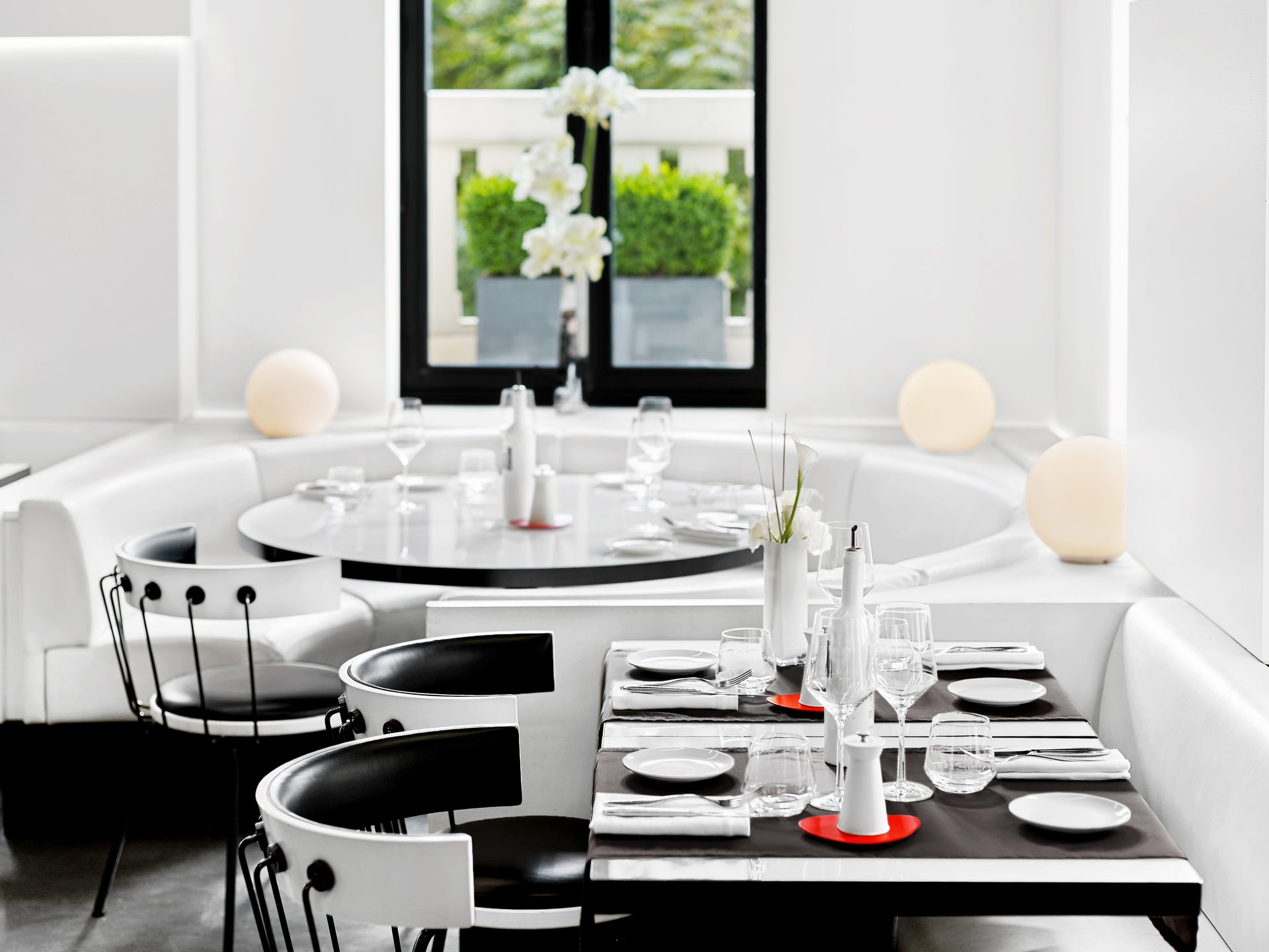Nolita Paris — vue 03 — vue rapprochée de l'angle banquette, table ronde et table rectangulaire dressées, signal rouge des dessous-de-plats Galateo & Friends