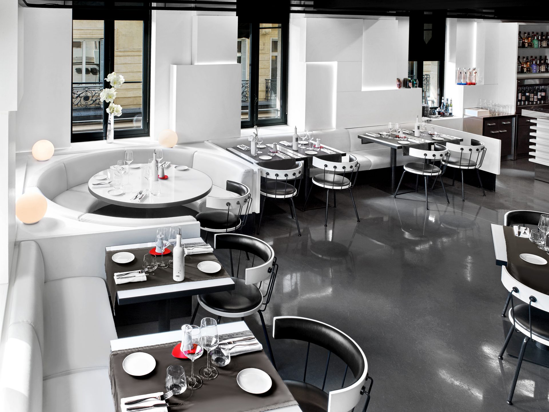 Nolita Paris — vue 14 — vue plongeante sur la salle haute, sol miroir noir et mobilier circulaire blanc, lampe Pipistrello jaune au bar du fond