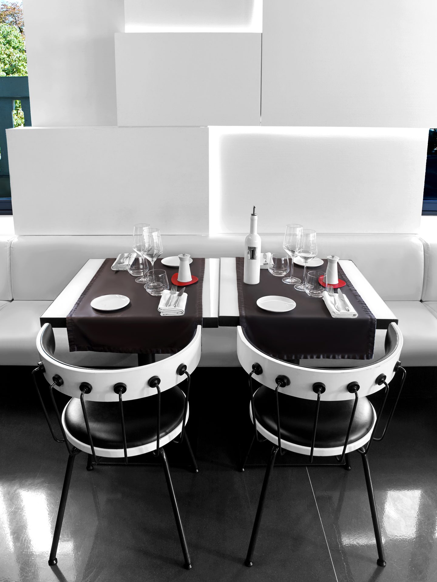 Nolita Paris — vue 21 — cadrage vertical sur tables jumelles en alcôve, banquettes blanches et sol miroir, fenêtre lumineuse en arrière-plan