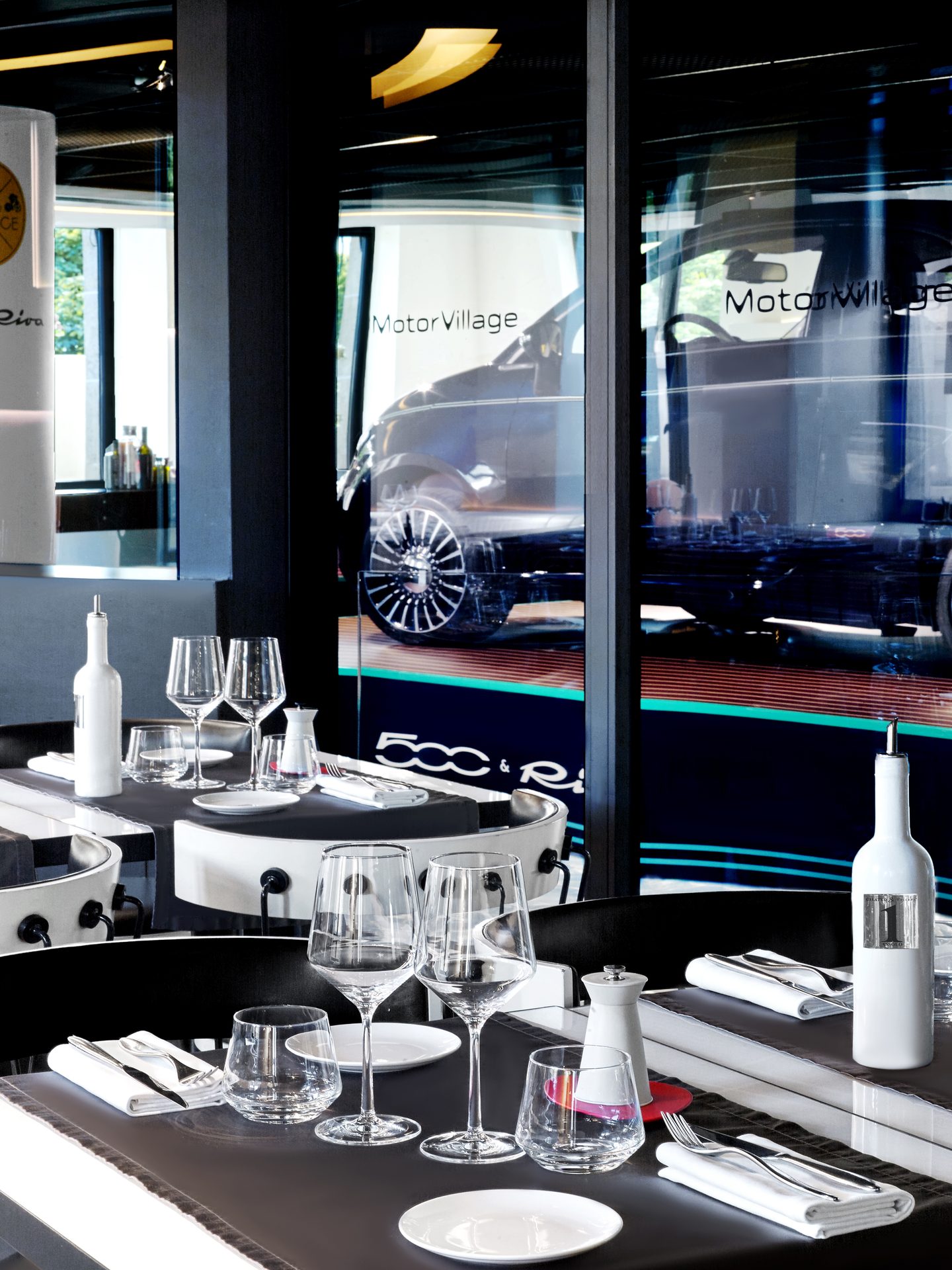 Nolita Paris — vue 30 — cadrage vertical sur l'enfilade de tables vers l'alcôve Fiat 500 & Riva, voiture bleue visible au fond