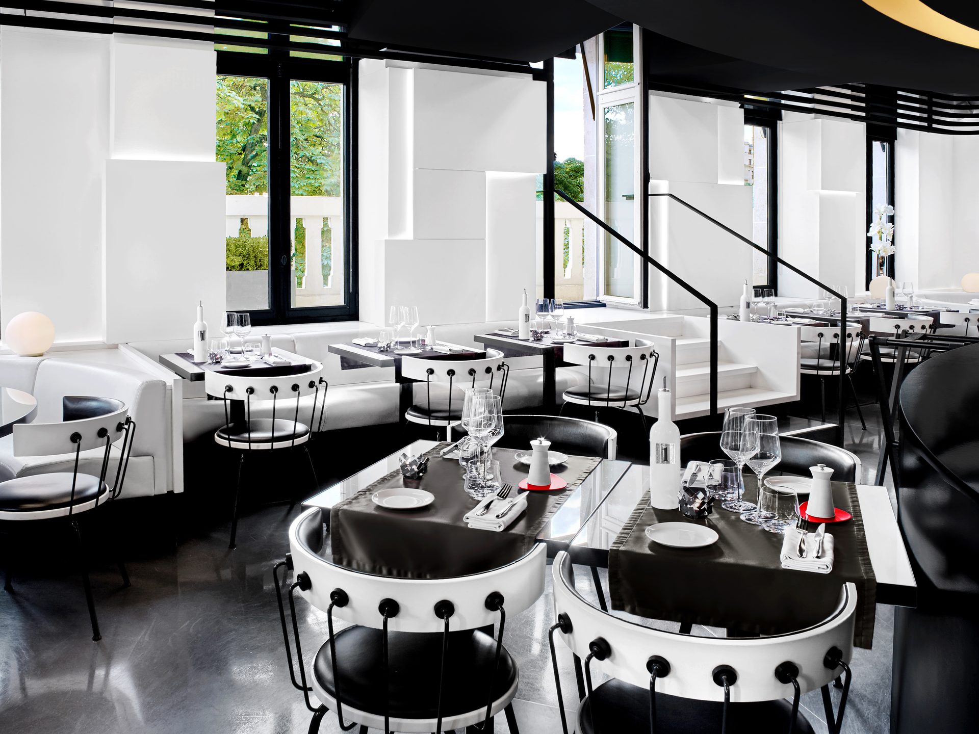 Nolita Paris — vue 33 — mezzanine niveau bas, tables près de l'escalier et chaises sur estrade, baies vitrées sur arbres du Triangle d'Or