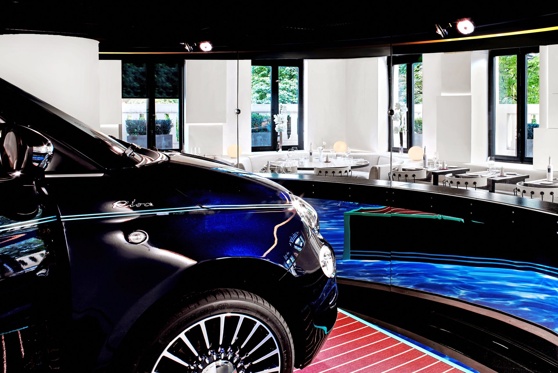Nolita Paris — vue 37 — alcôve Fiat 500 vue depuis la salle, reflet de la Fiat noire dans la vitrine, tables blanches cloutées au premier plan et lettrage FIAT en miroir