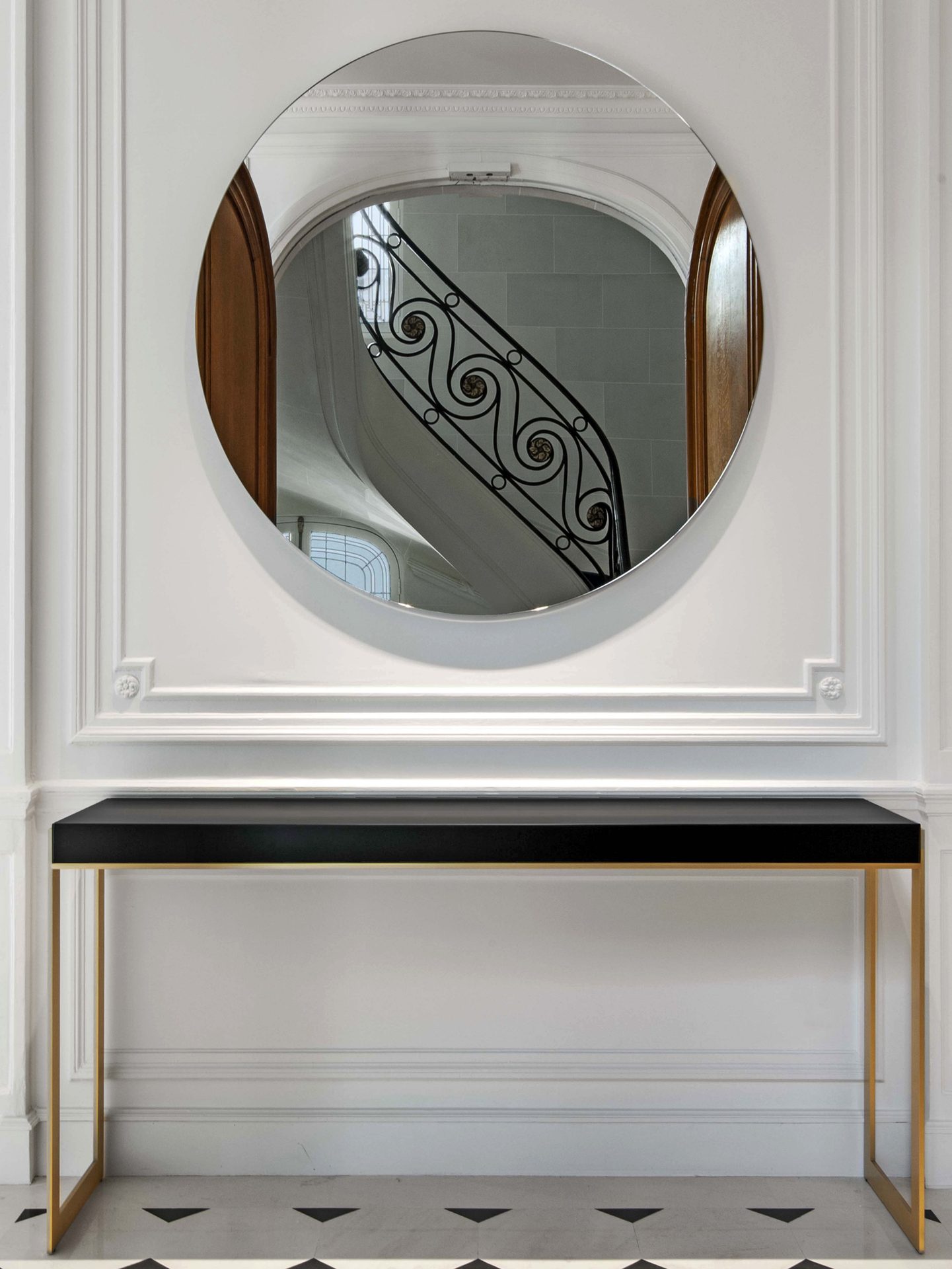 Appartement au Trocadéro — vue 01 — miroir rond mural reflétant l'escalier en fer forgé, console noire et laiton, sol damier marbre noir et blanc