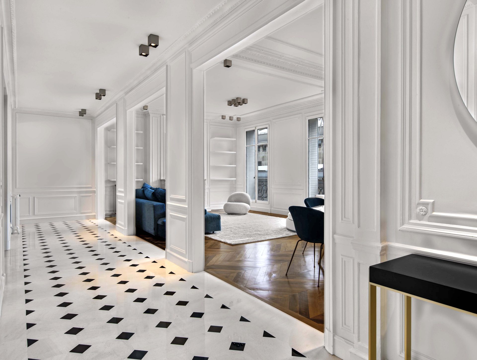 Appartement au Trocadéro — vue 02 — enfilade des pièces en perspective, sol marbre à cabochons noirs, salon avec fauteuils velours bleu nuit