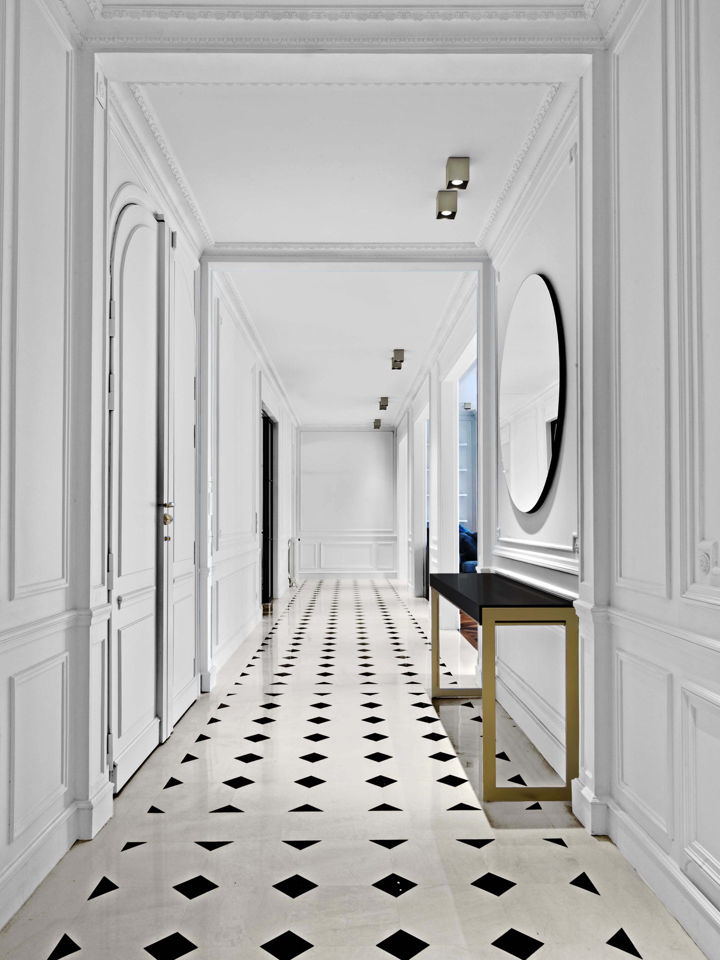 Appartement au Trocadéro — vue 03 — galerie de distribution, sol damier marbre noir et blanc, console laiton et miroir rond, boiseries blanches