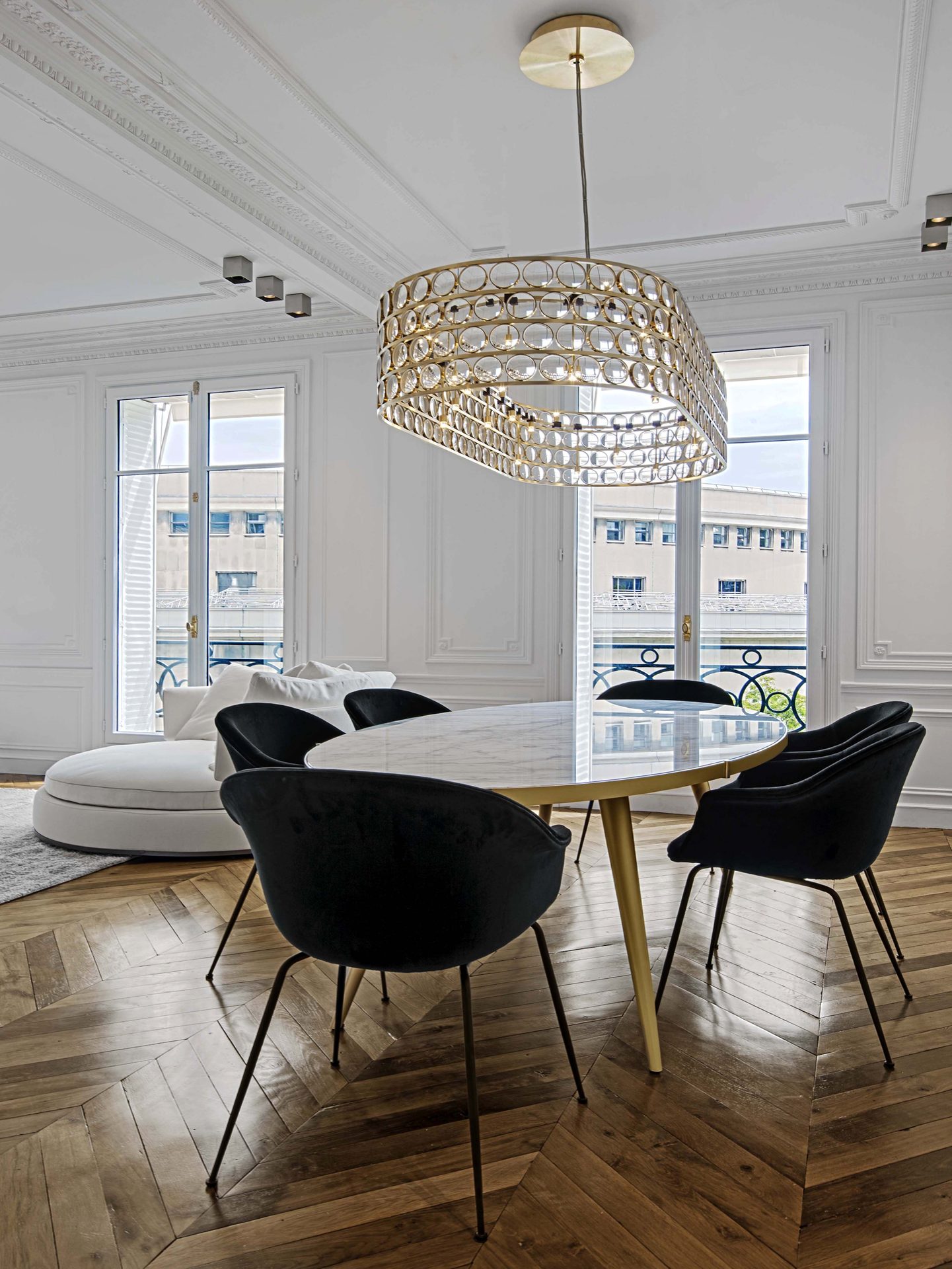 Appartement au Trocadéro — vue 04 — salle à manger, table ovale en marbre et piètement laiton, chaises velours noir, lustre annulaire en laiton