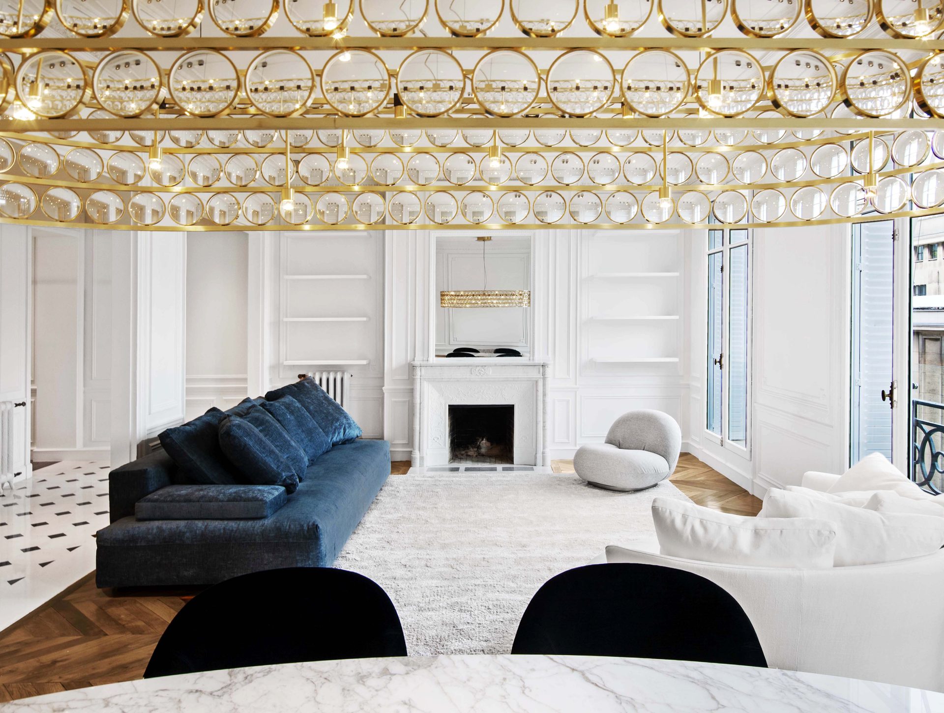 Appartement au Trocadéro — vue 05 — séjour vu sous le lustre à pastilles de verre et laiton, canapés bleu et blanc, cheminée en marbre blanc