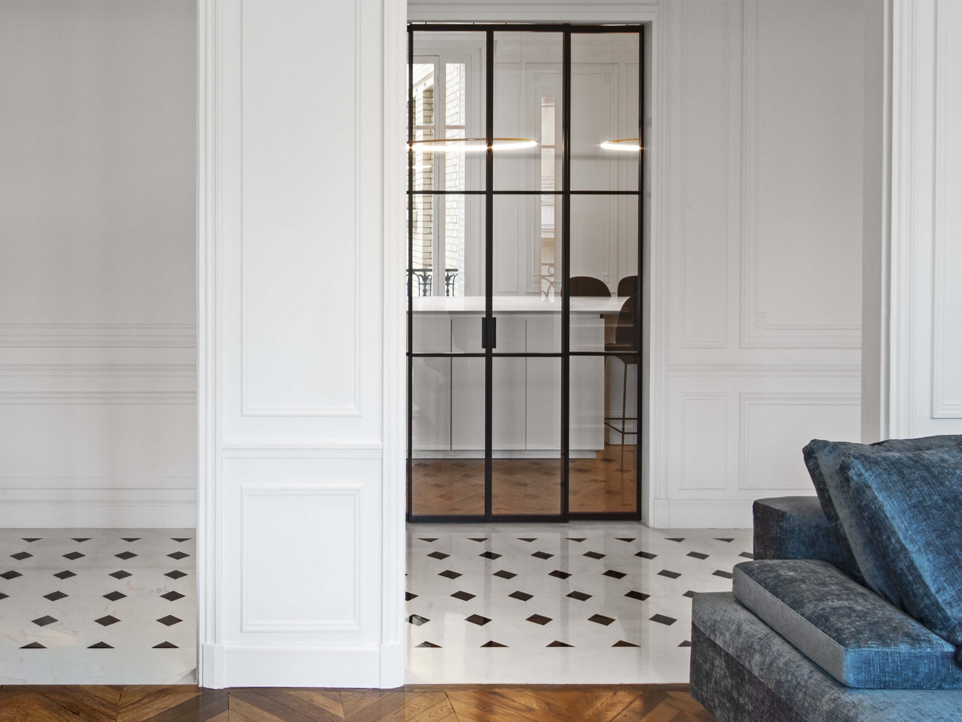 Appartement au Trocadéro — vue 09 — verrière atelier noire entre séjour et cuisine, sol marbre à cabochons, canapé velours bleu