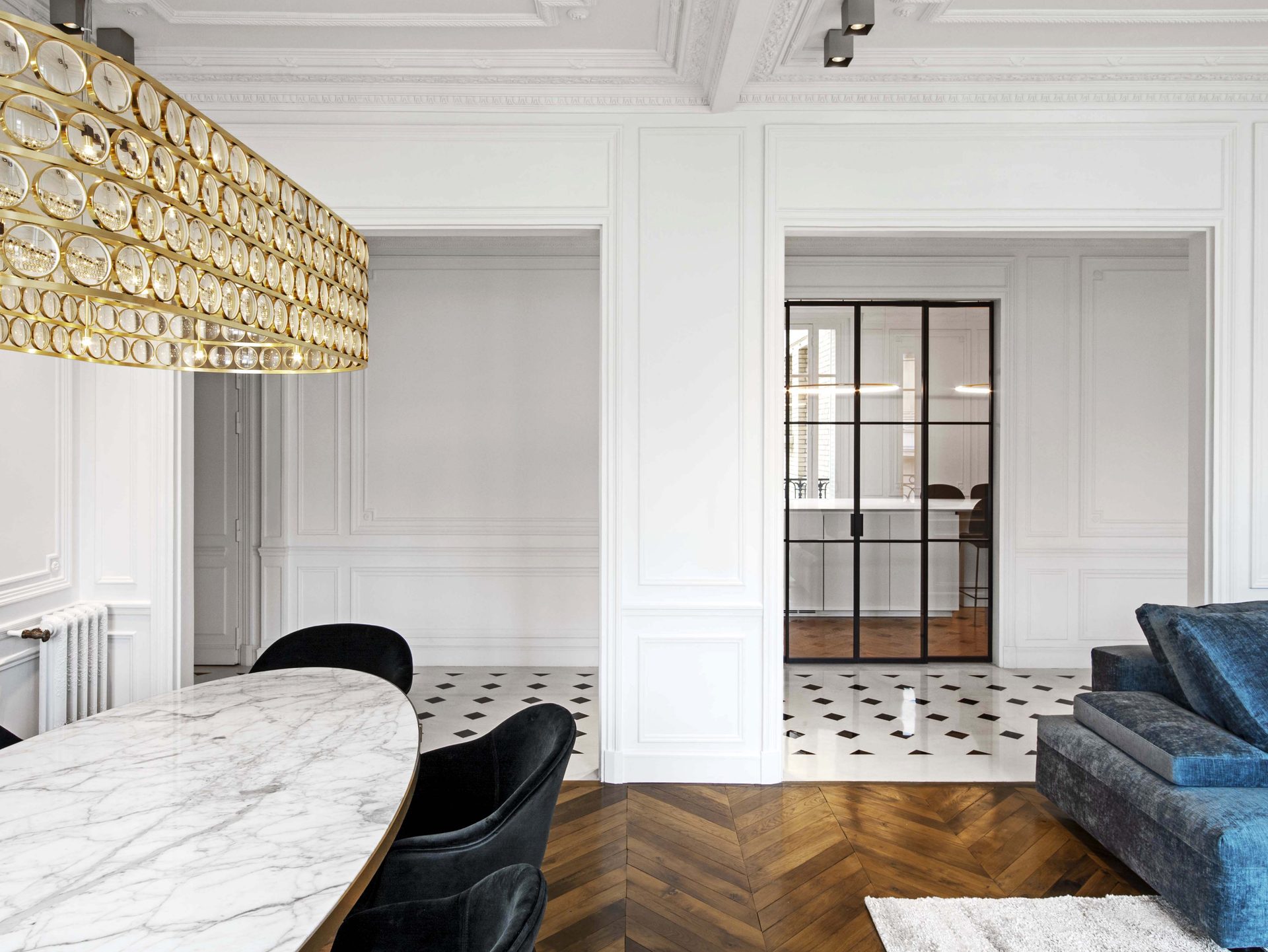 Appartement au Trocadéro — vue 11 — séjour-salle à manger, lustre laiton, double porte sur galerie, parquet chevrons et tapis clair