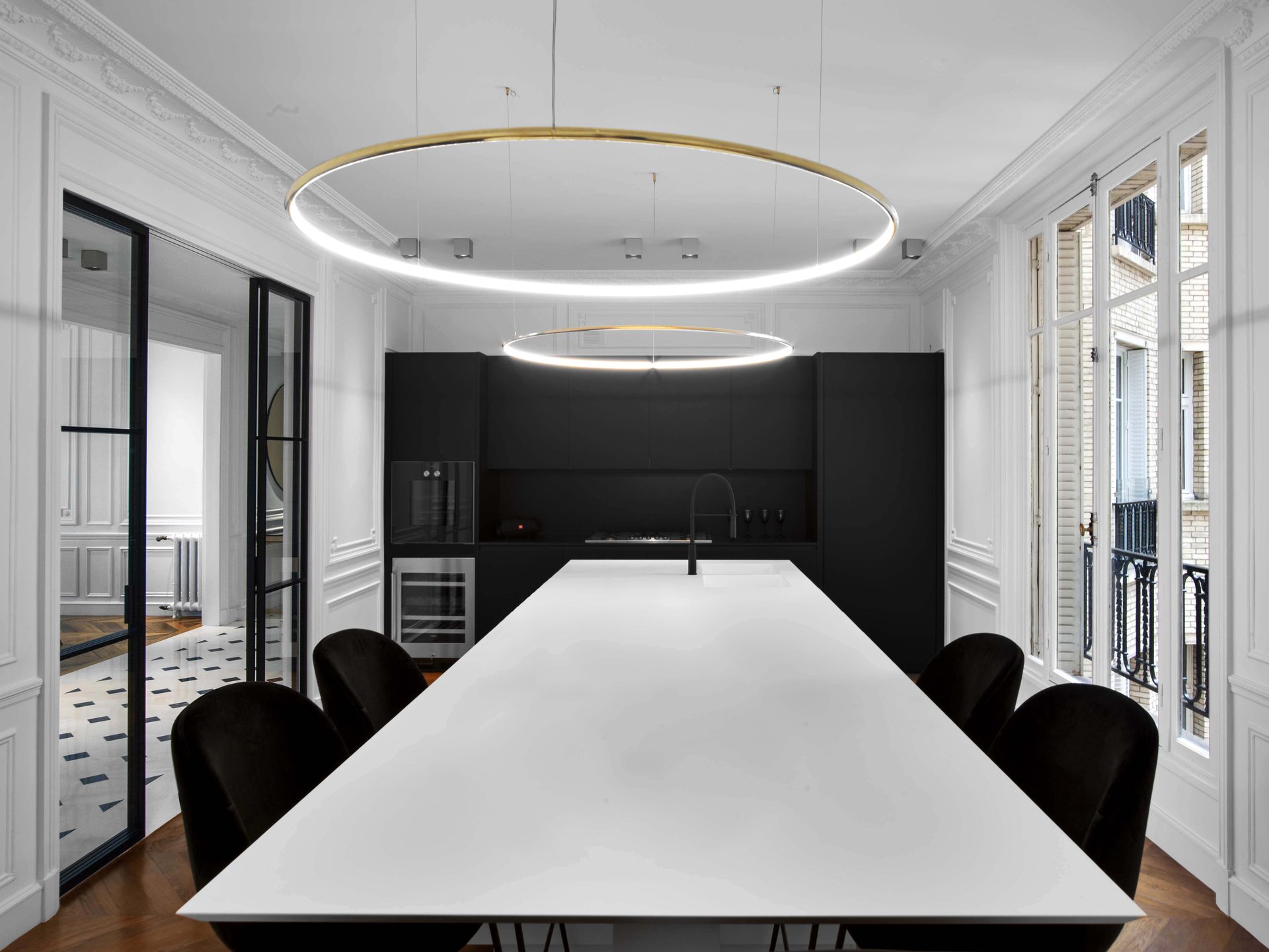 Appartement au Trocadéro — vue 16 — cuisine noire et îlot blanc, double anneau lumineux suspendu, verrière et fenêtres sur rue