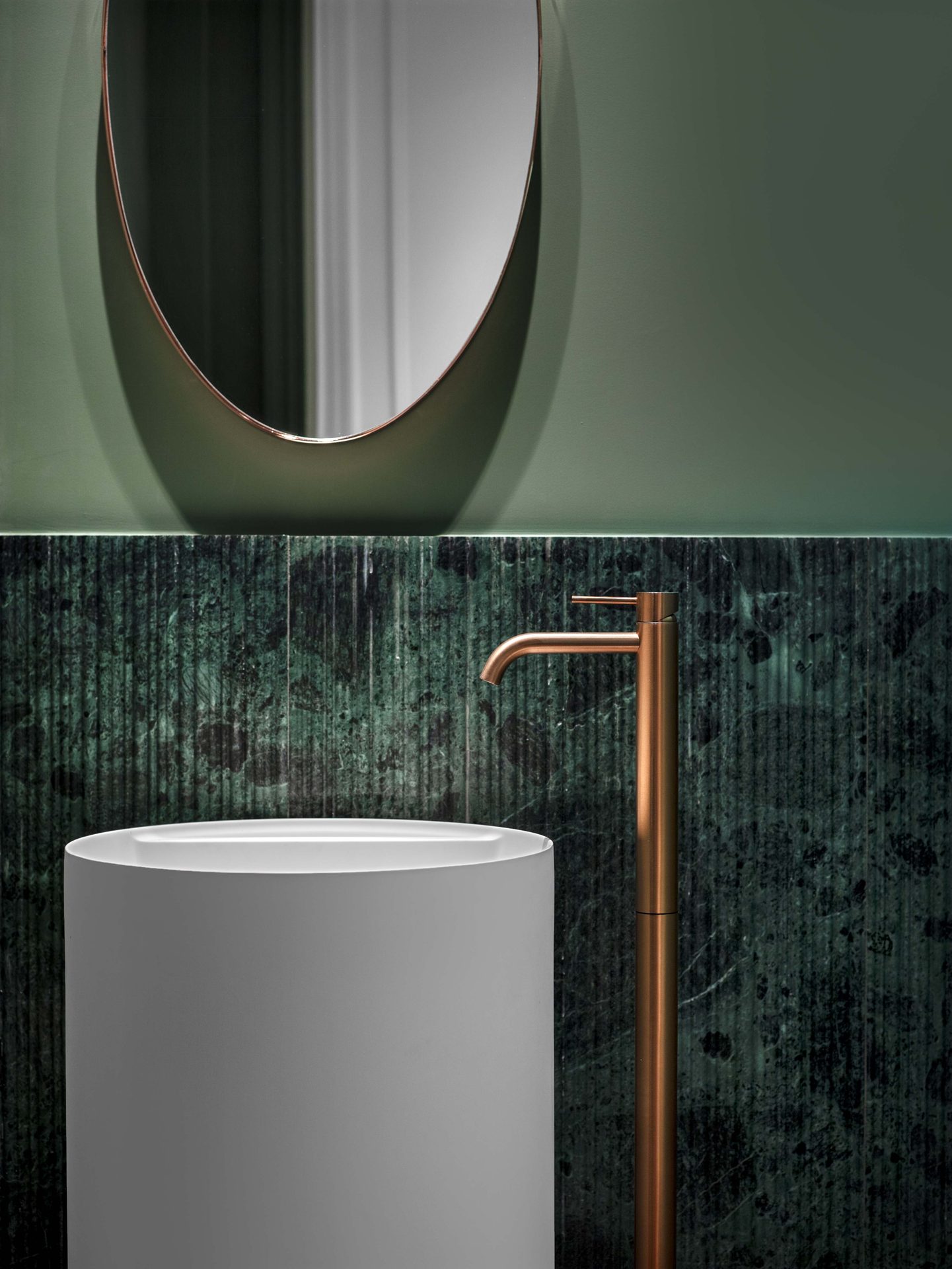Appartement au Trocadéro — vue 29 — toilettes d'invités, vasque colonne blanche, mitigeur cuivre sur fond de marbre vert veiné, miroir ovale