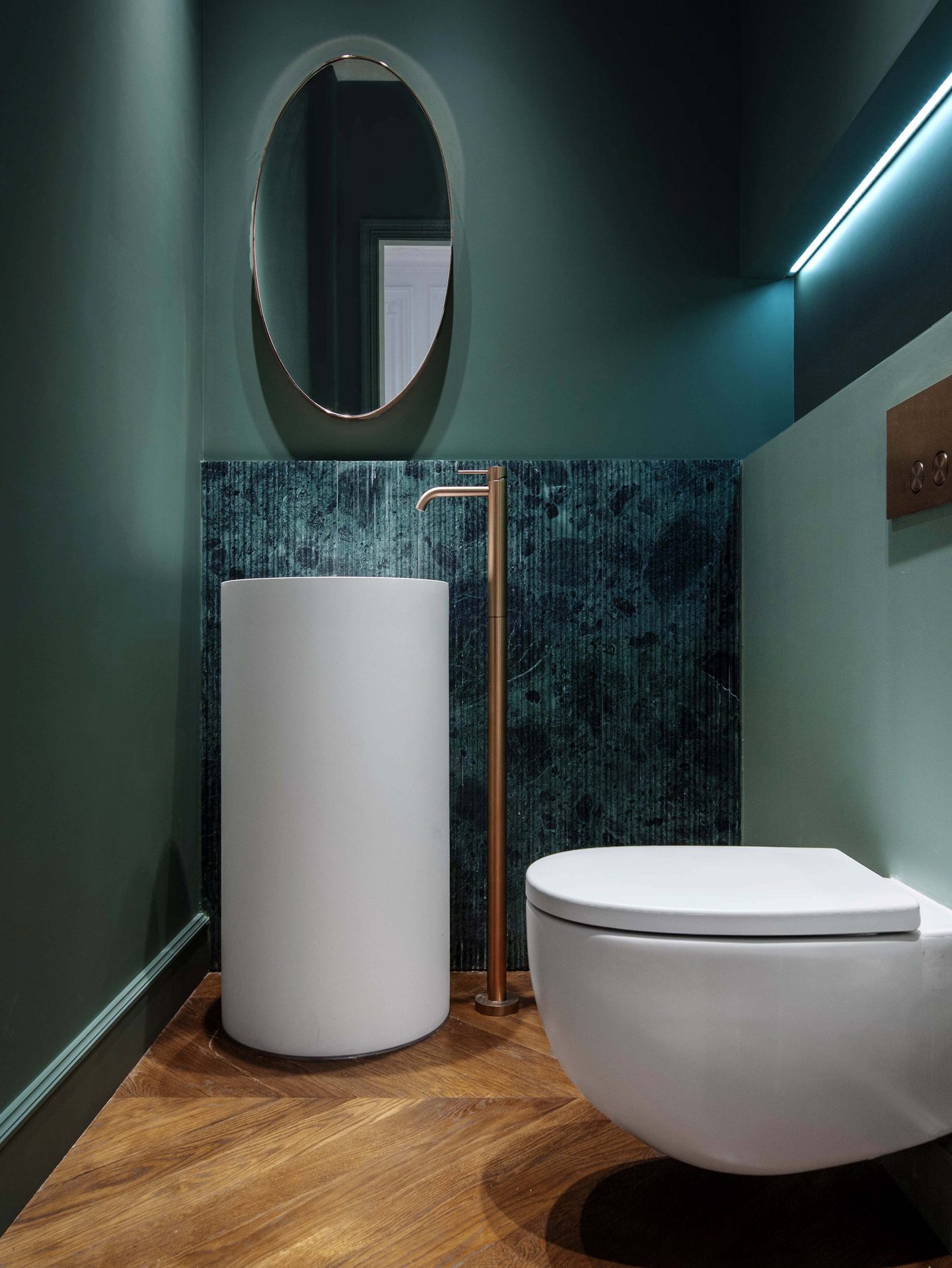 Appartement au Trocadéro — vue 33 — toilettes d'invités en vert profond, vasque colonne, WC suspendu, sol parquet, miroir ovale