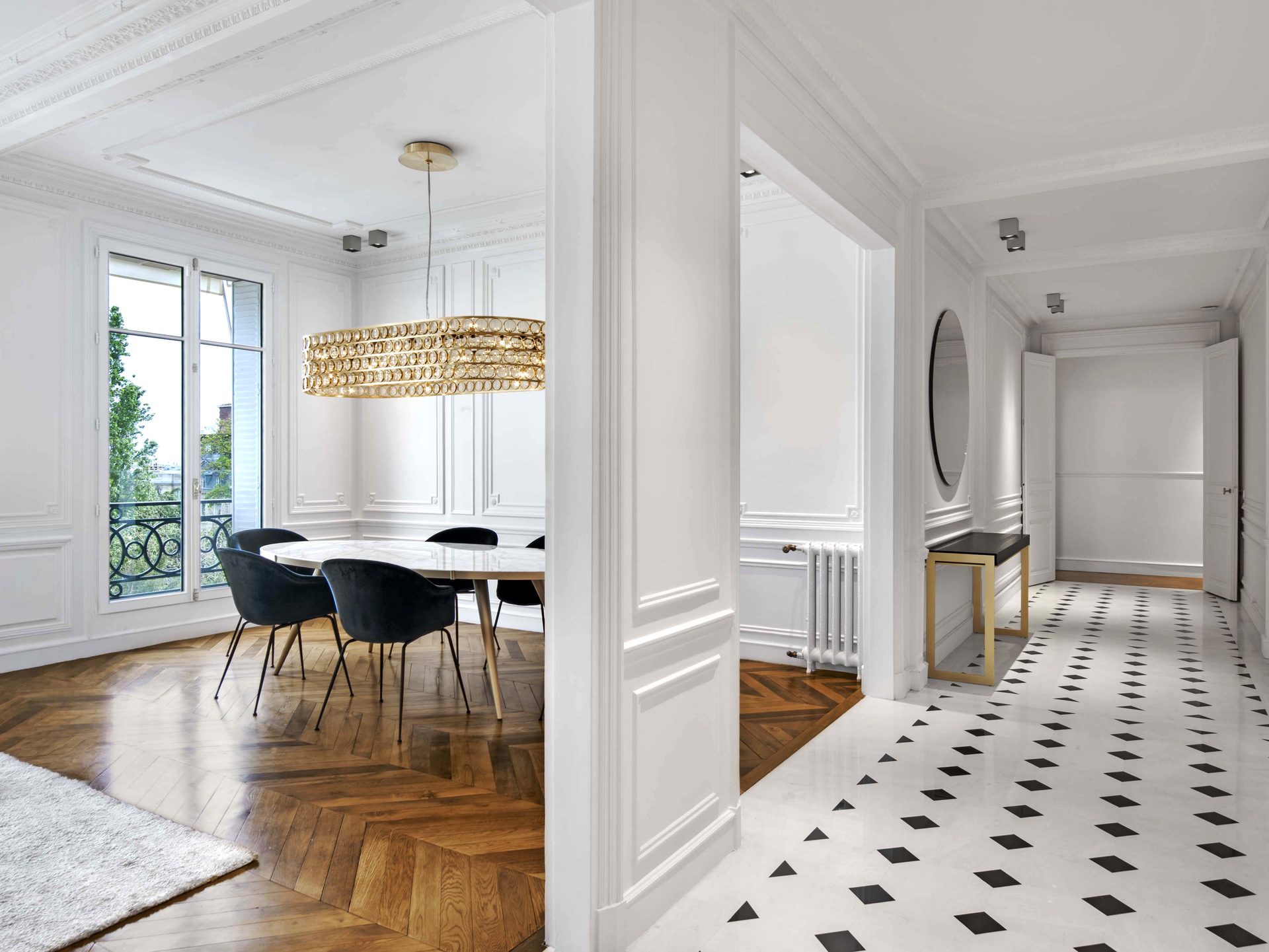 Appartement au Trocadéro — vue 40 — salle à manger et galerie, table marbre, lustre laiton à pastilles, sol damier, fenêtre sur les arbres