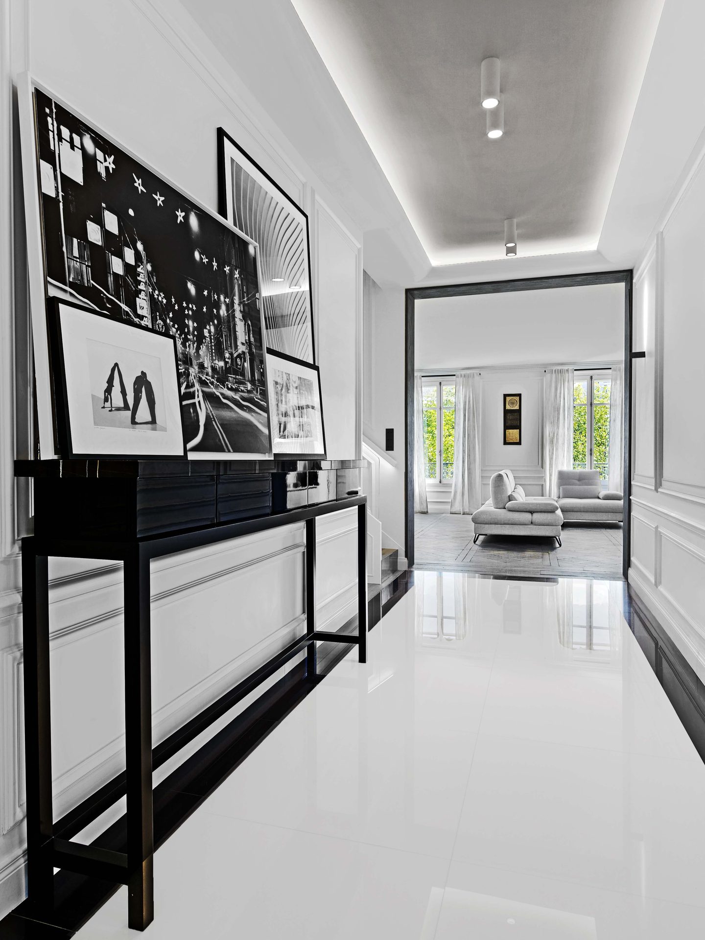 Pereire — vue 01 — galerie d'entrée, sol laqué blanc brillant, console noire et collection de photographies noir et blanc encadrées, enfilade vers le salon clair