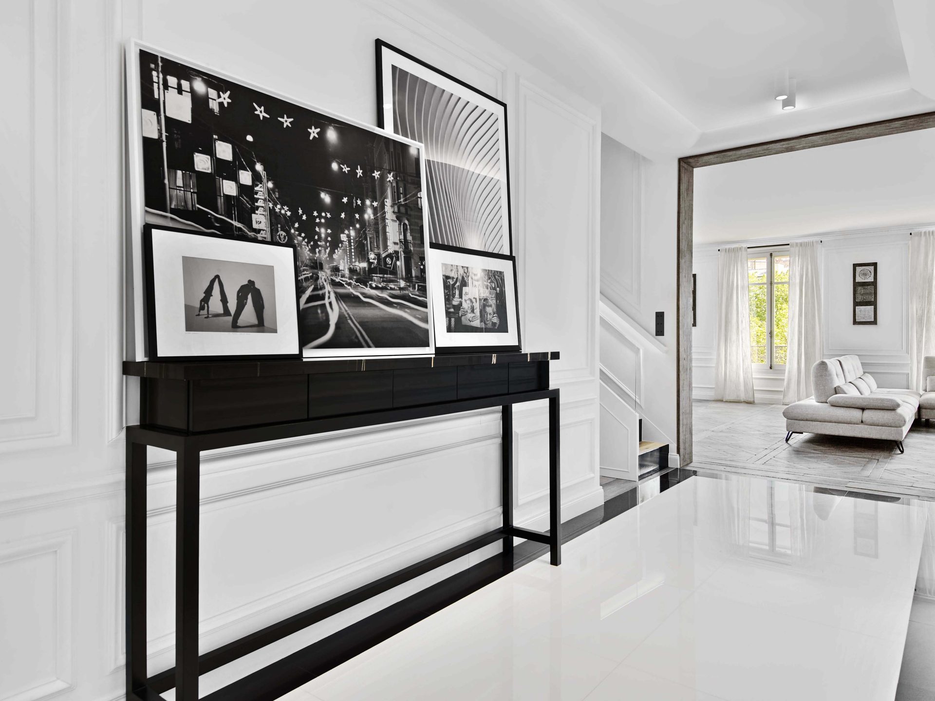 Pereire — vue 03 — vue d'ensemble de la galerie d'entrée, sol blanc miroir, mur de photographies noir et blanc, perspective vers le salon