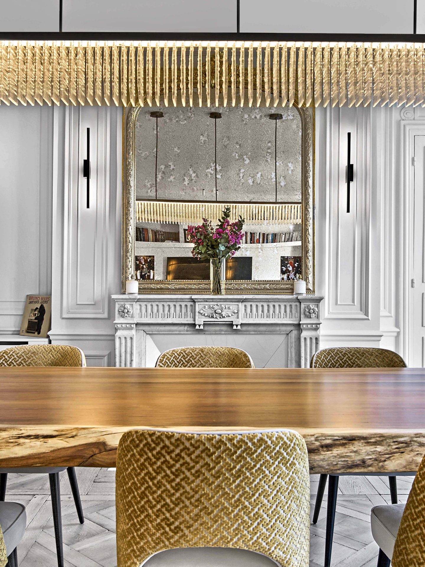 Pereire — vue 12 — détail de la table live-edge et des chaises moutarde face au miroir doré piqué et à la cheminée de marbre blanc