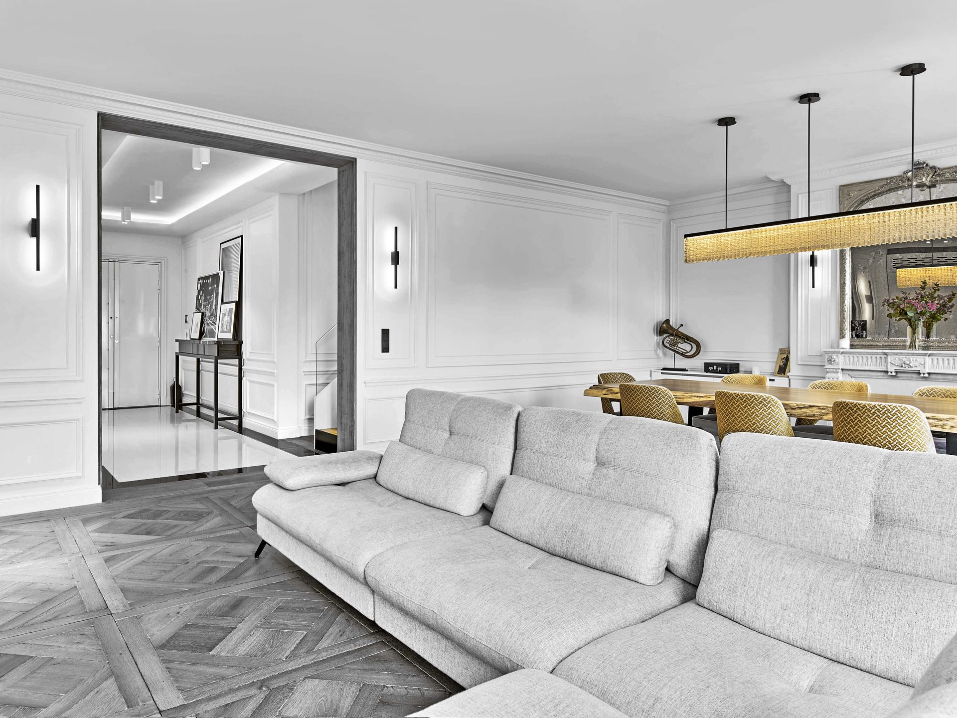 Pereire — vue 14 — séjour, canapé gris clair et table en bois brut, suspension linéaire dorée, enfilade vers la galerie d'entrée laquée