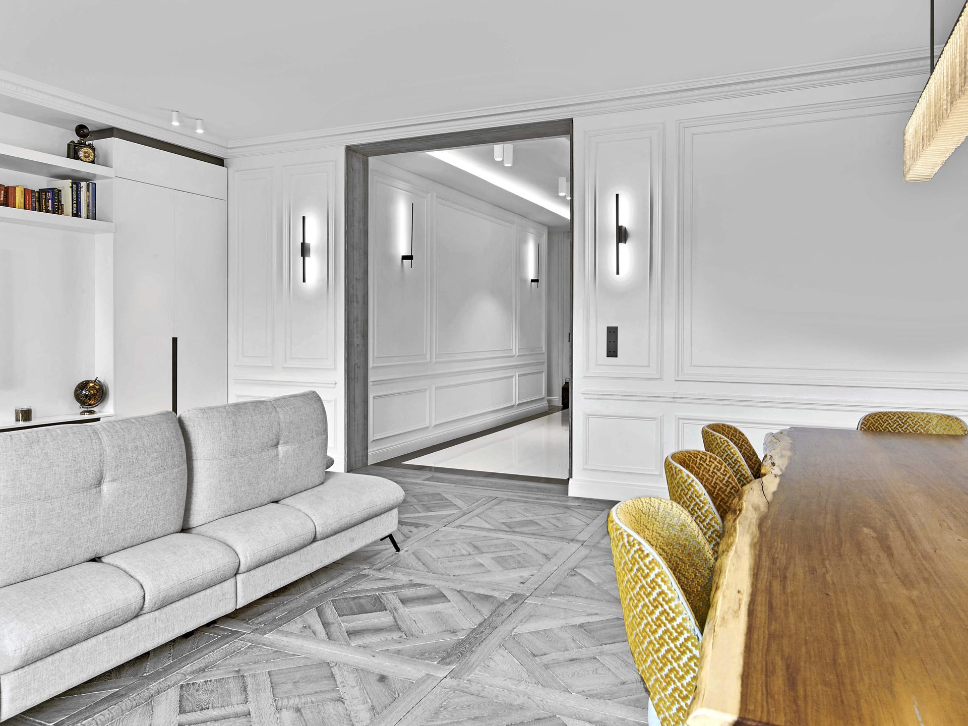 Pereire — vue 16 — séjour ouvert sur le couloir à boiseries, appliques noires verticales, parquet point de Hongrie, canapé gris