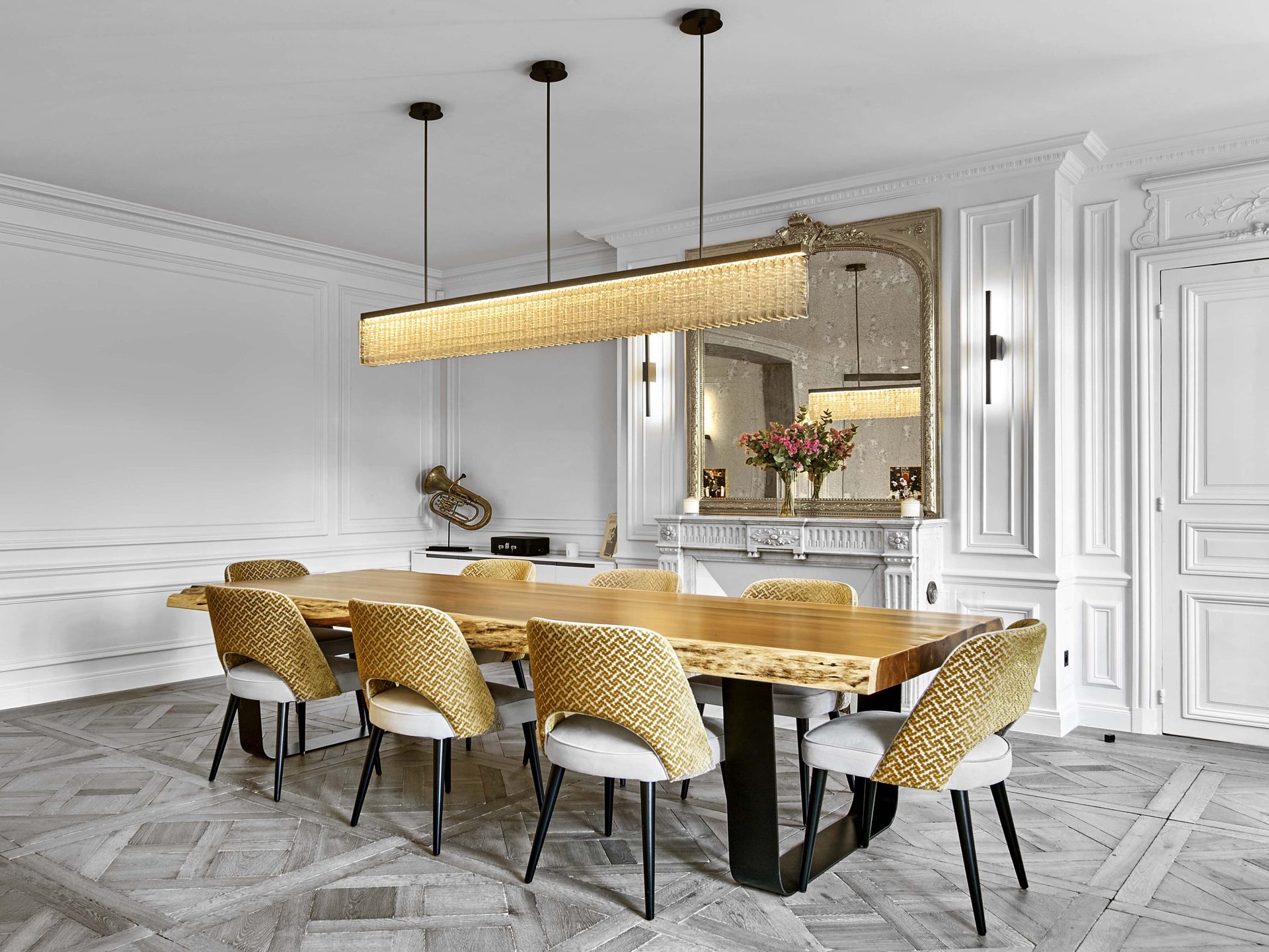Pereire — vue 22 — salle à manger, table en bois brut à bord naturel, chaises tissées moutarde, longue suspension de verre dorée, miroir doré ancien sur cheminée de marbre