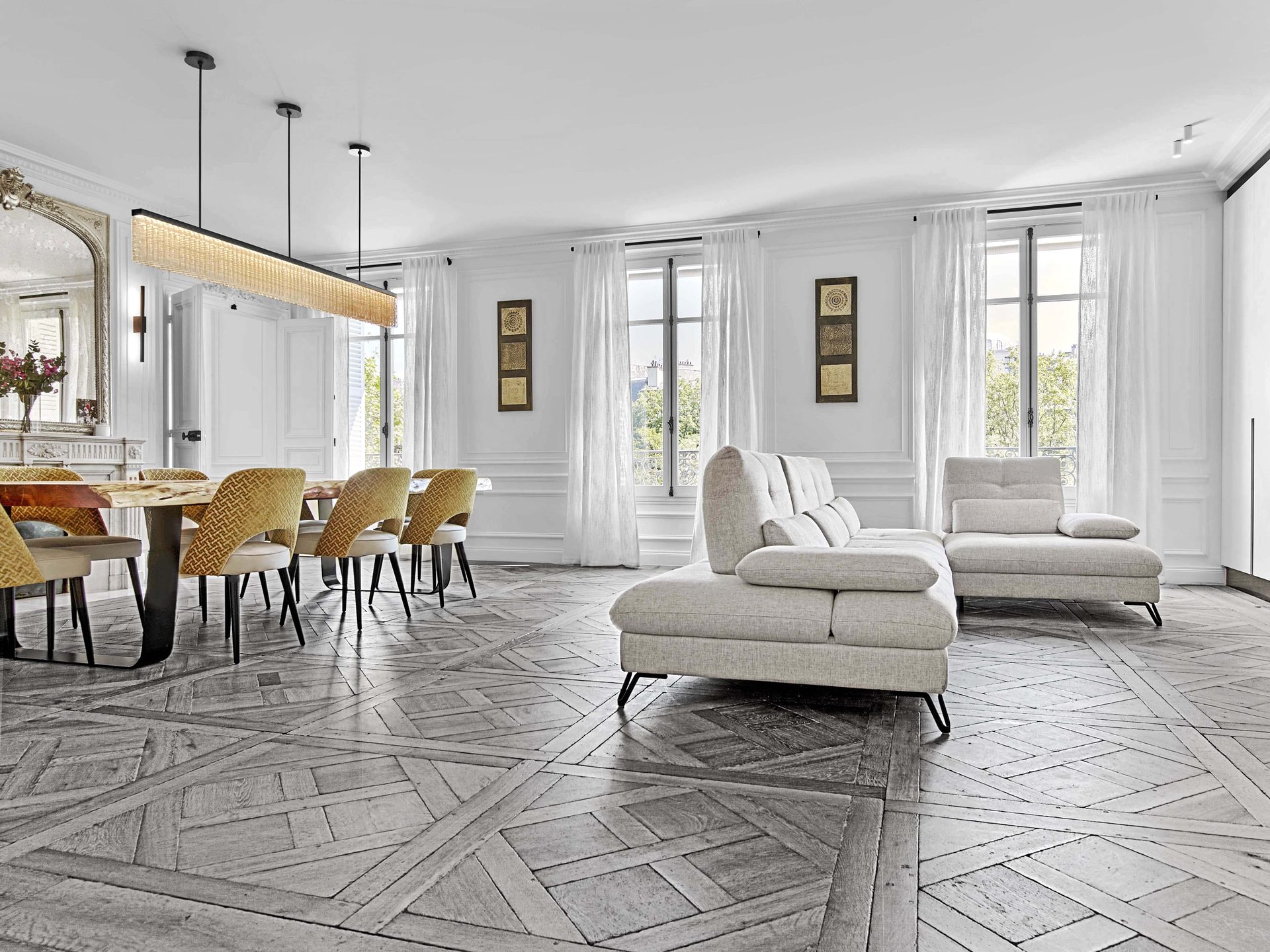 Pereire — vue 23 — double séjour ouvert, parquet de Versailles, canapés gris et table à manger, grandes fenêtres à voilages blancs, œuvres dorées encadrées