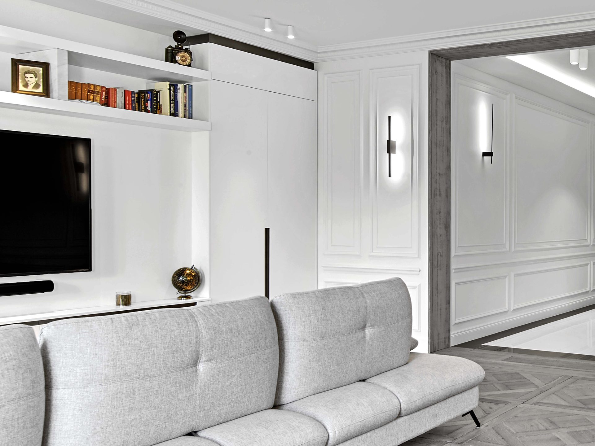 Pereire — vue 25 — séjour, canapé gris, mur TV et bibliothèque laqués blancs, cloison à boiseries avec porte coulissante et appliques noires verticales
