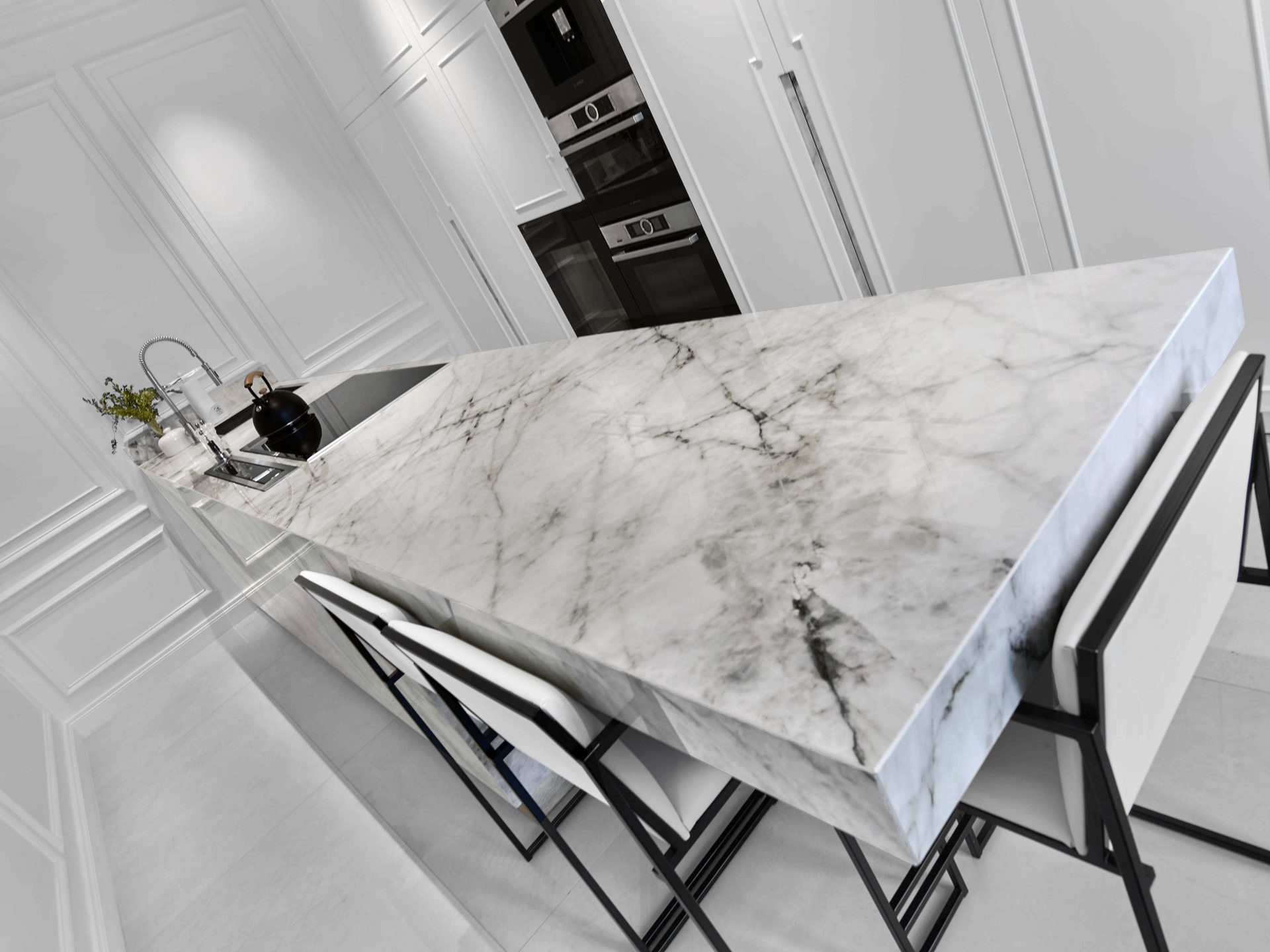 Pereire — vue 35 — îlot de cuisine en marbre vu en perspective dynamique, plan de cuisson à induction et colonne de fours en fond