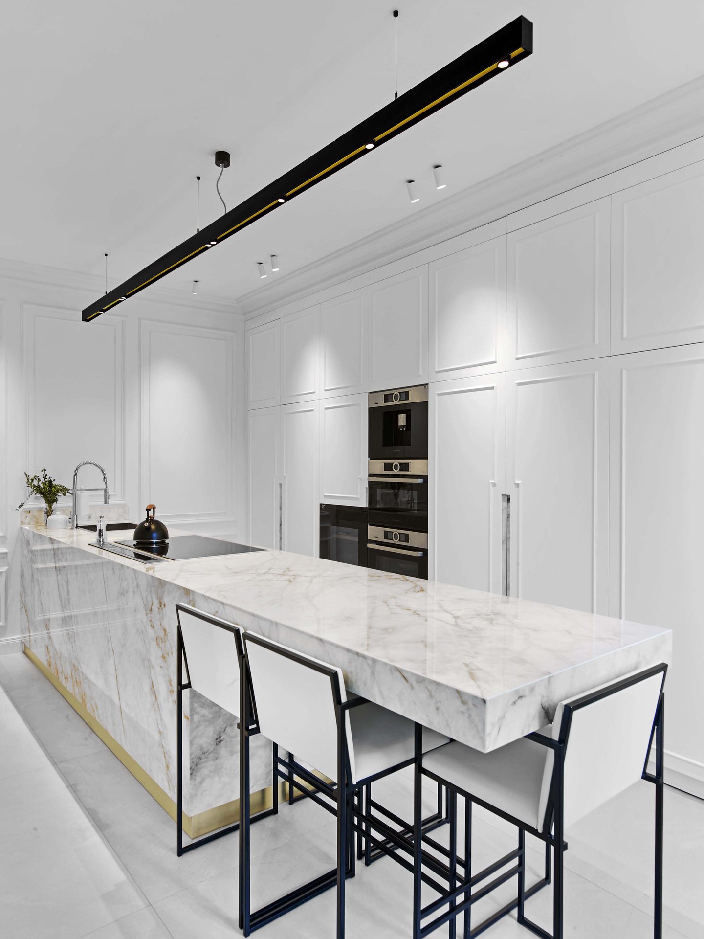 Pereire — vue 37 — cuisine en hauteur, îlot de marbre et tabourets de bar, réglette suspendue noir et laiton, colonne de fours encastrés