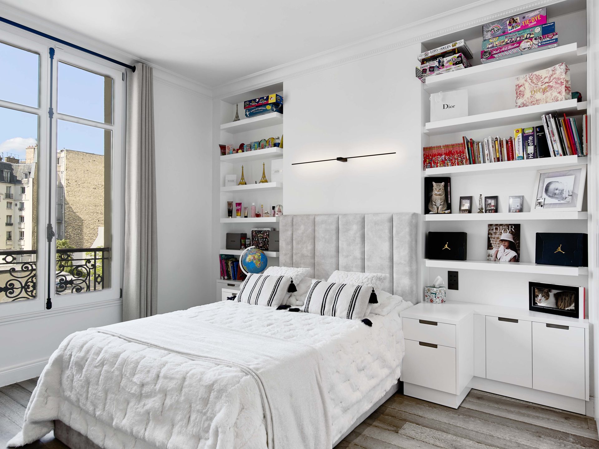 Pereire — vue 44 — chambre d'enfant, lit habillé de blanc, étagères blanches garnies de livres et objets, fenêtre à ferronnerie sur les toits de Paris