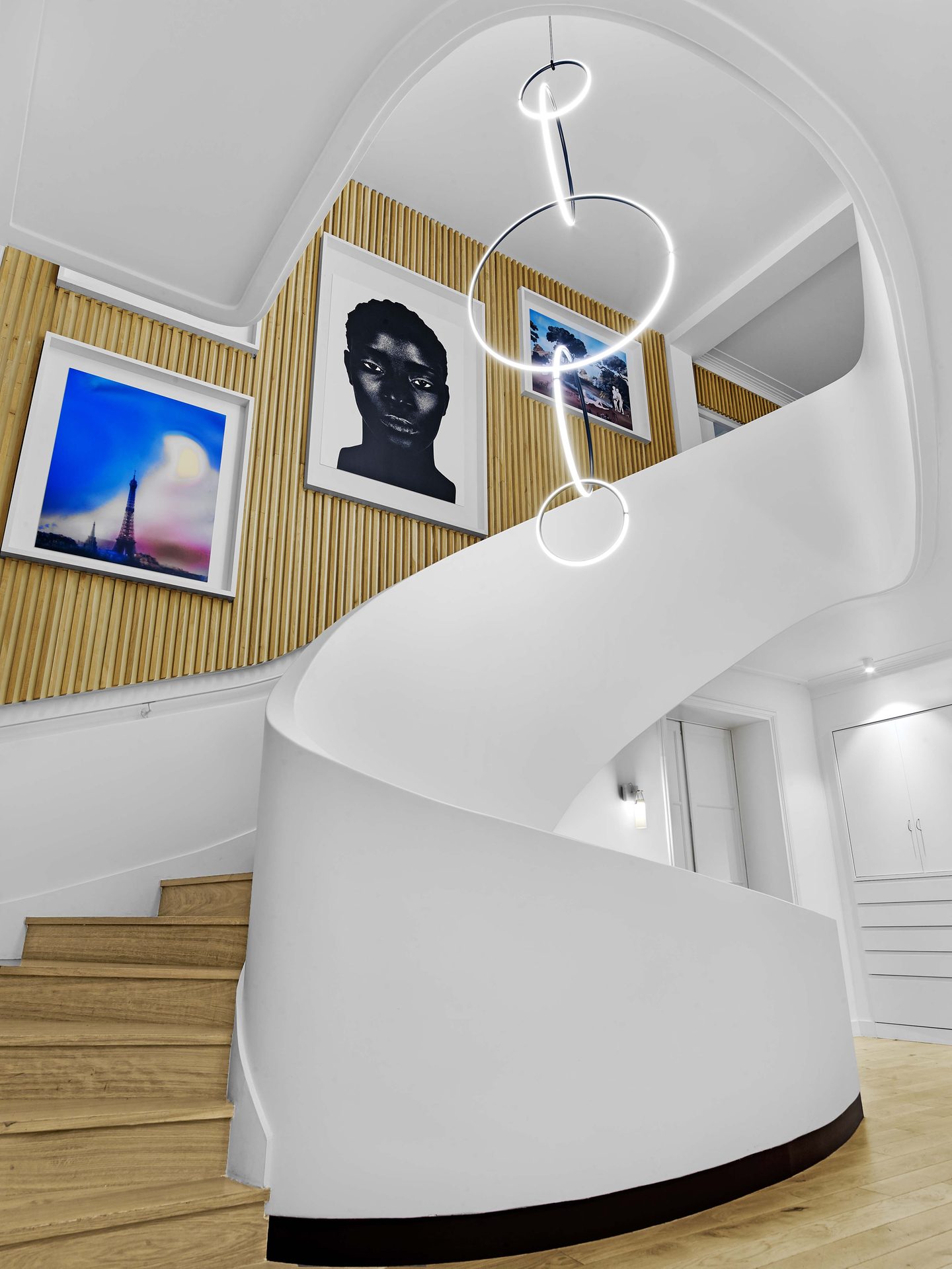 Beaux Arts — vue 04 — escalier blanc en spirale et œuvres encadrées sur mur de tasseaux de chêne