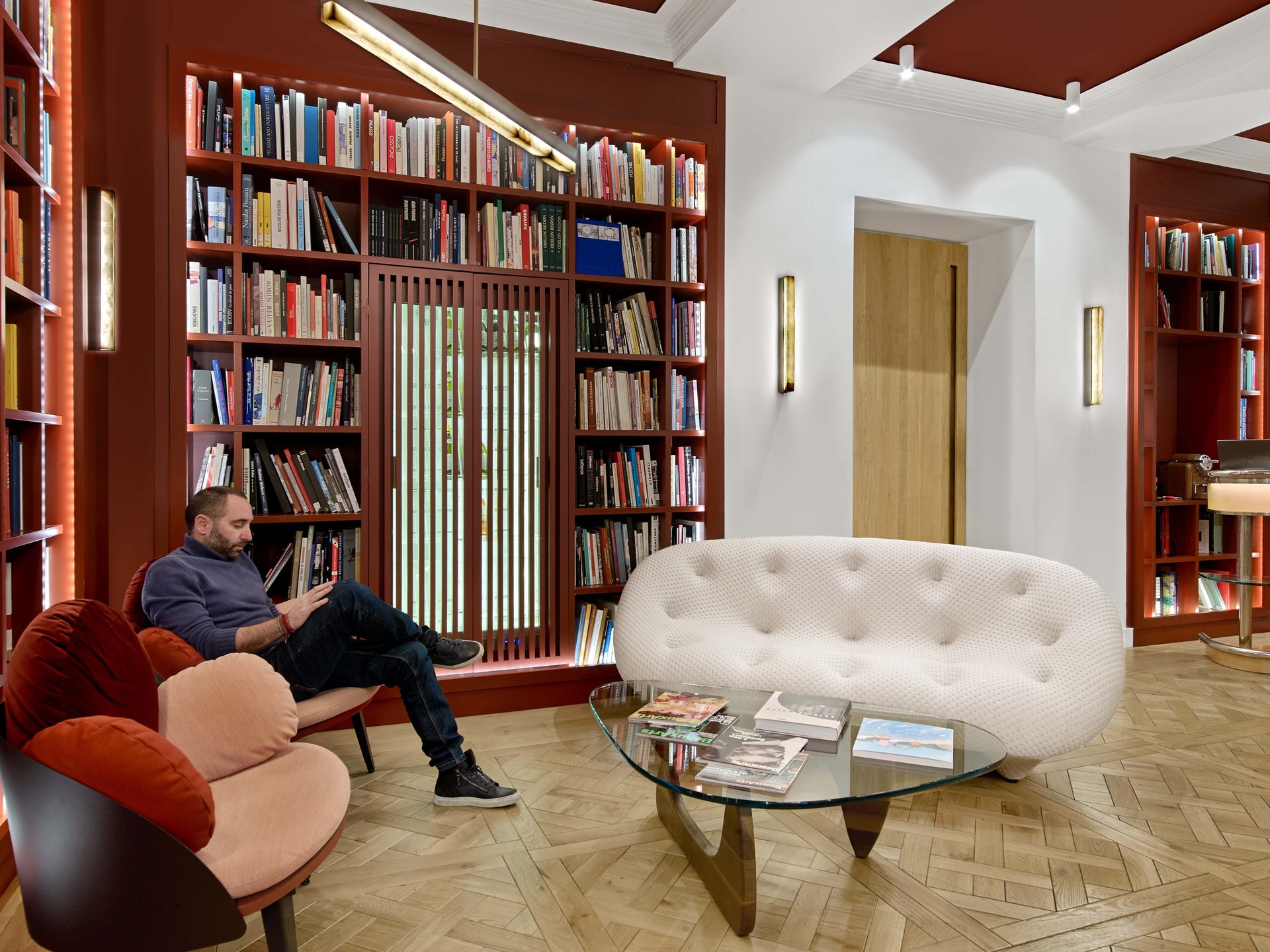 Beaux Arts — vue 60 — bibliothèque rouge profond, canapé blanc capitonné et livres d'art